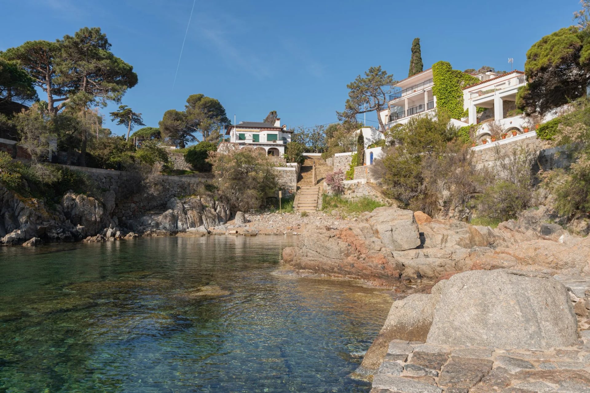 Small rocky cove with clear shallow water and white houses on the slope above