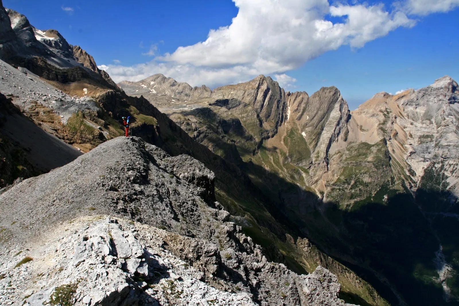 Walker high on a rocky shoulder with jagged limestone summits across the valley