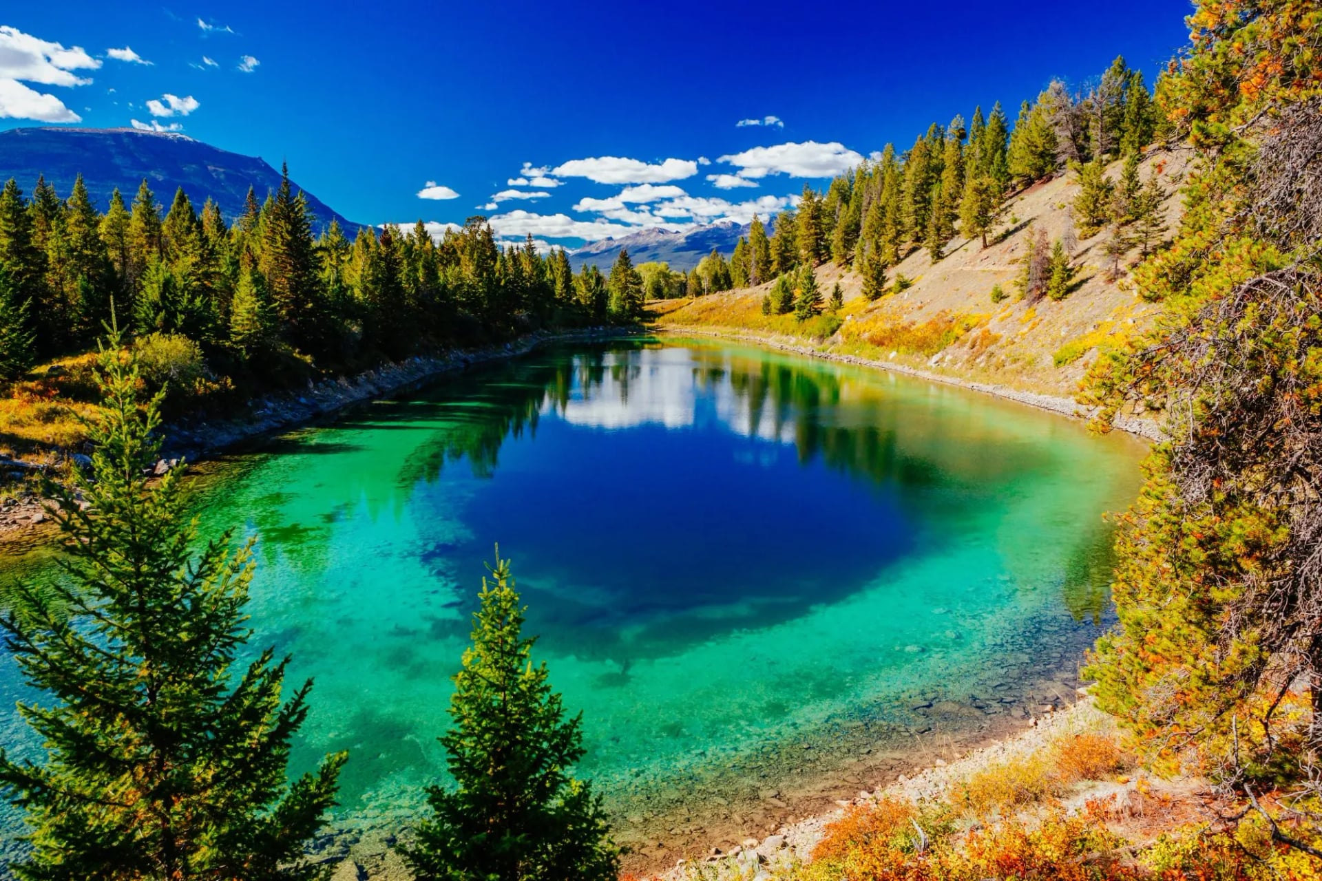 Vivid turquoise water at Third Lake framed by evergreens and autumn shrubs
