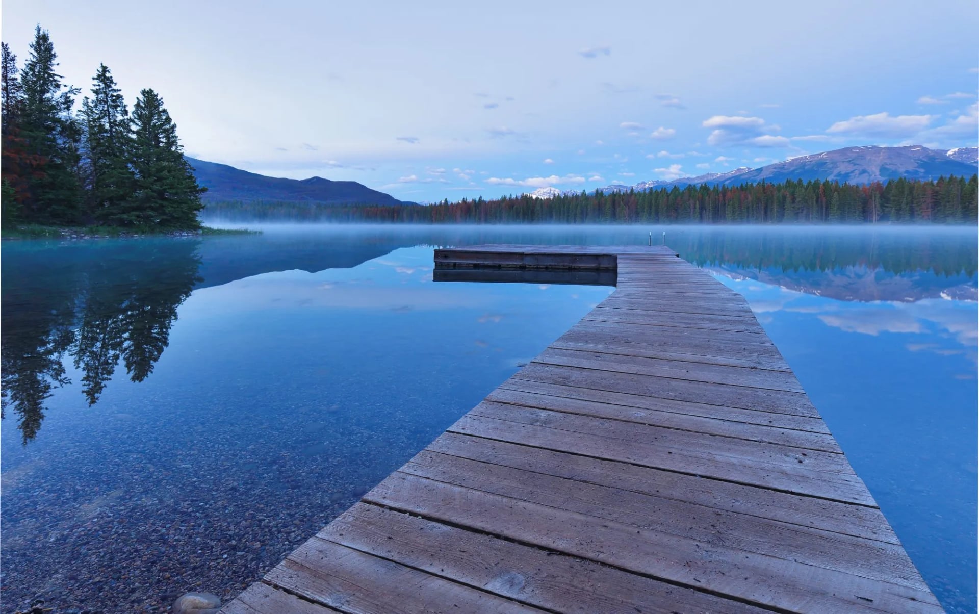 A wooden dock reaching into the flat calm water of Edith Lake under soft light