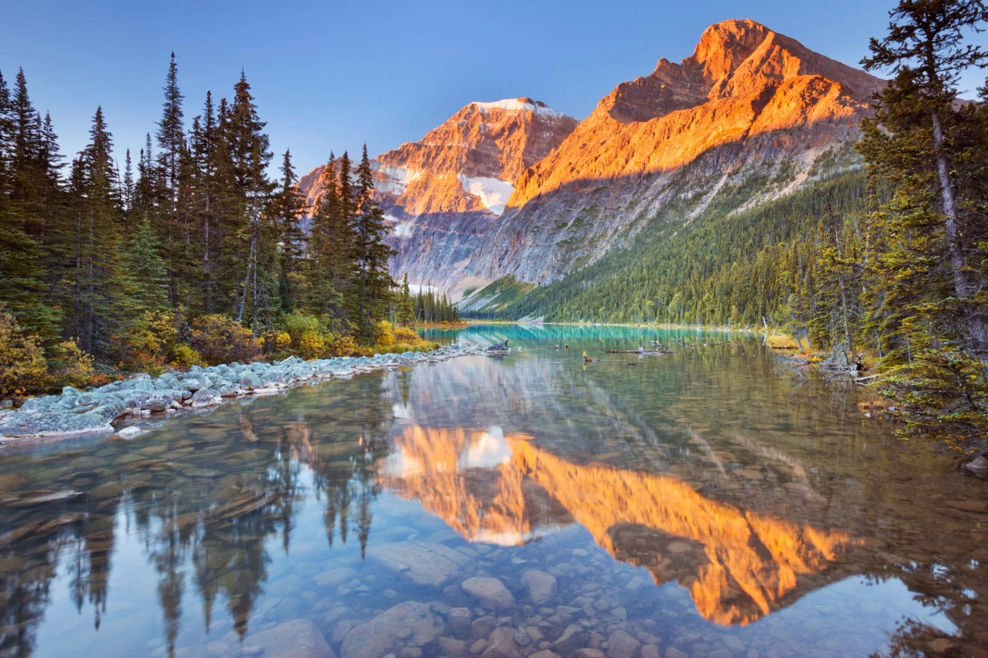Sunrise light on a peak reflected in the still water of Edith Lake