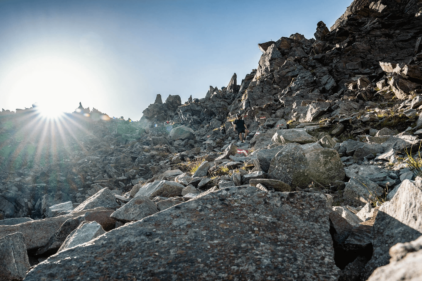 Hiker walking on a rocky mountain trail in the Stubai Alps with bright sun flare.