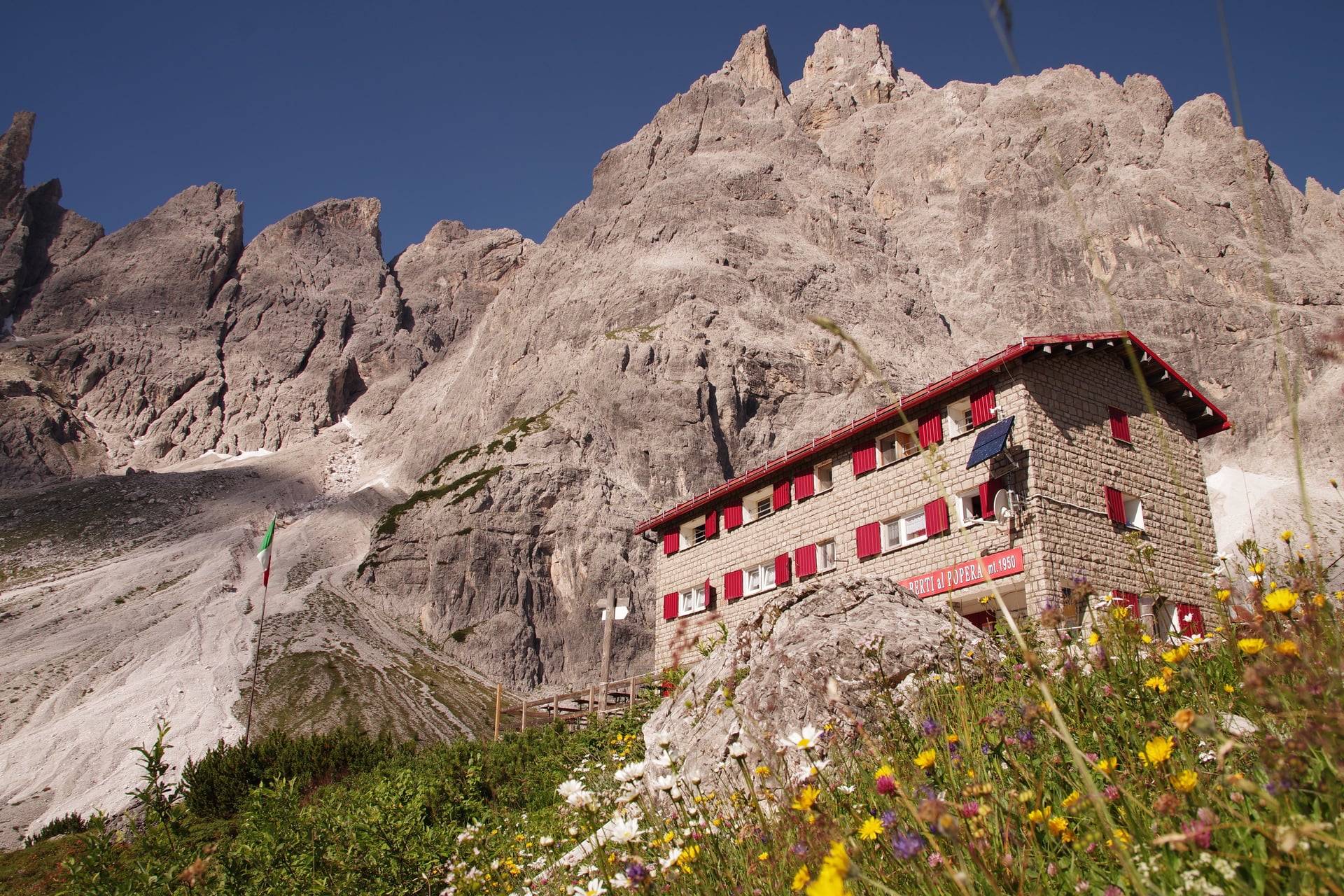 Refuge Berti avec volets rouges et fleurs sauvages dans les Dolomites italiennes.