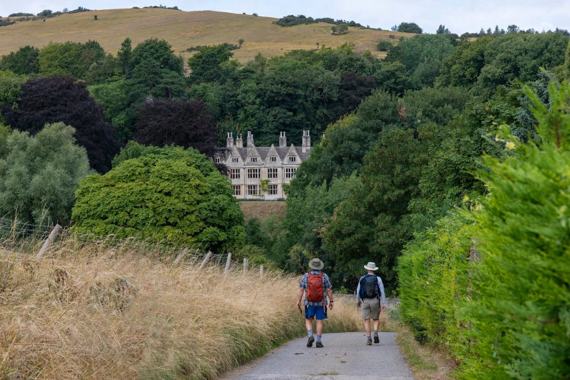 Two walkers with daypacks on a lane below an English country house