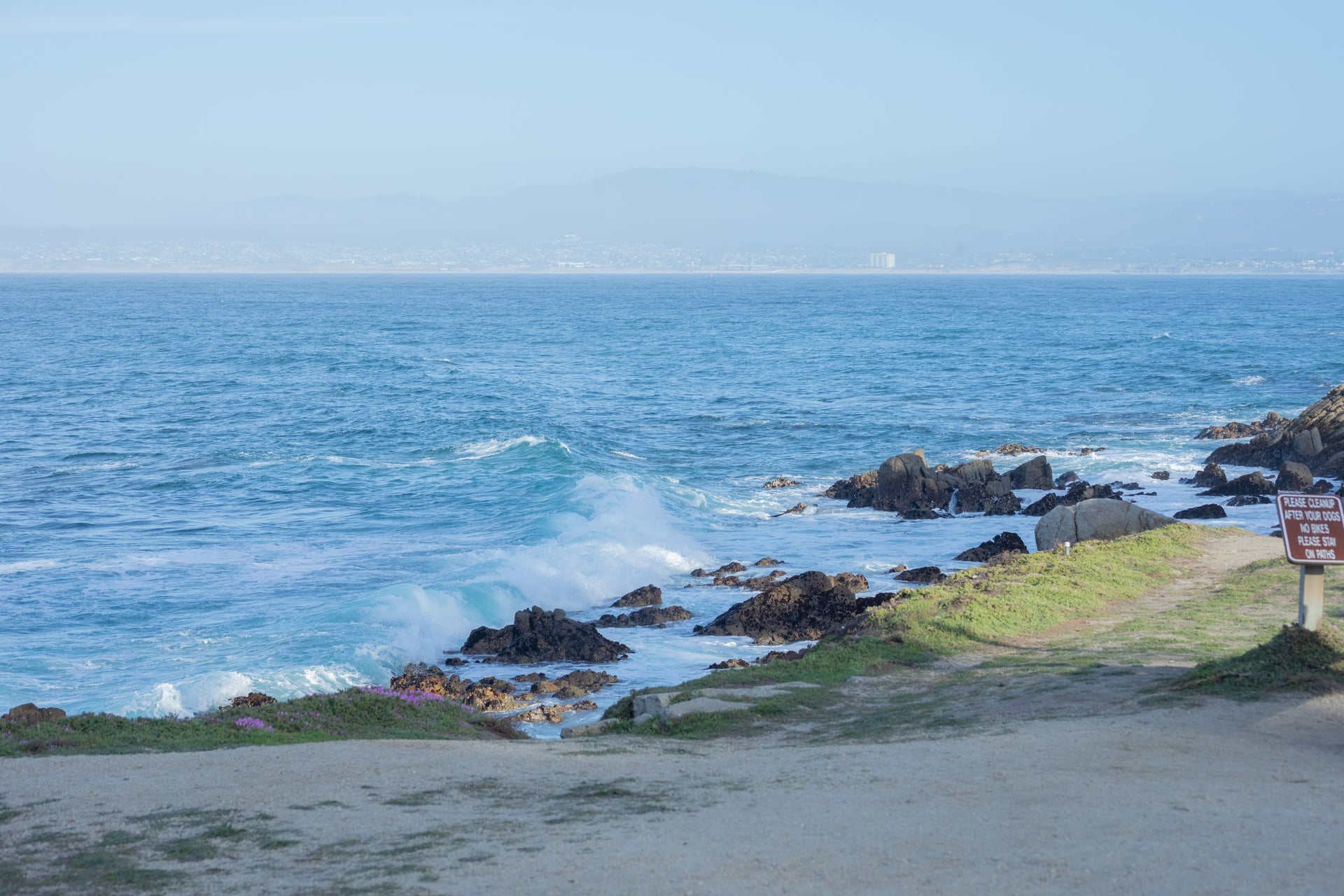 Surf breaking on the rocks of the Monterey coastline under a pale sky