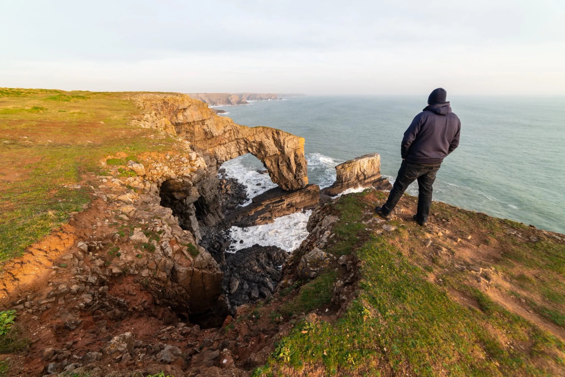 A walker looking out over the Green Bridge of Wales sea arch on the Pembrokeshire coast