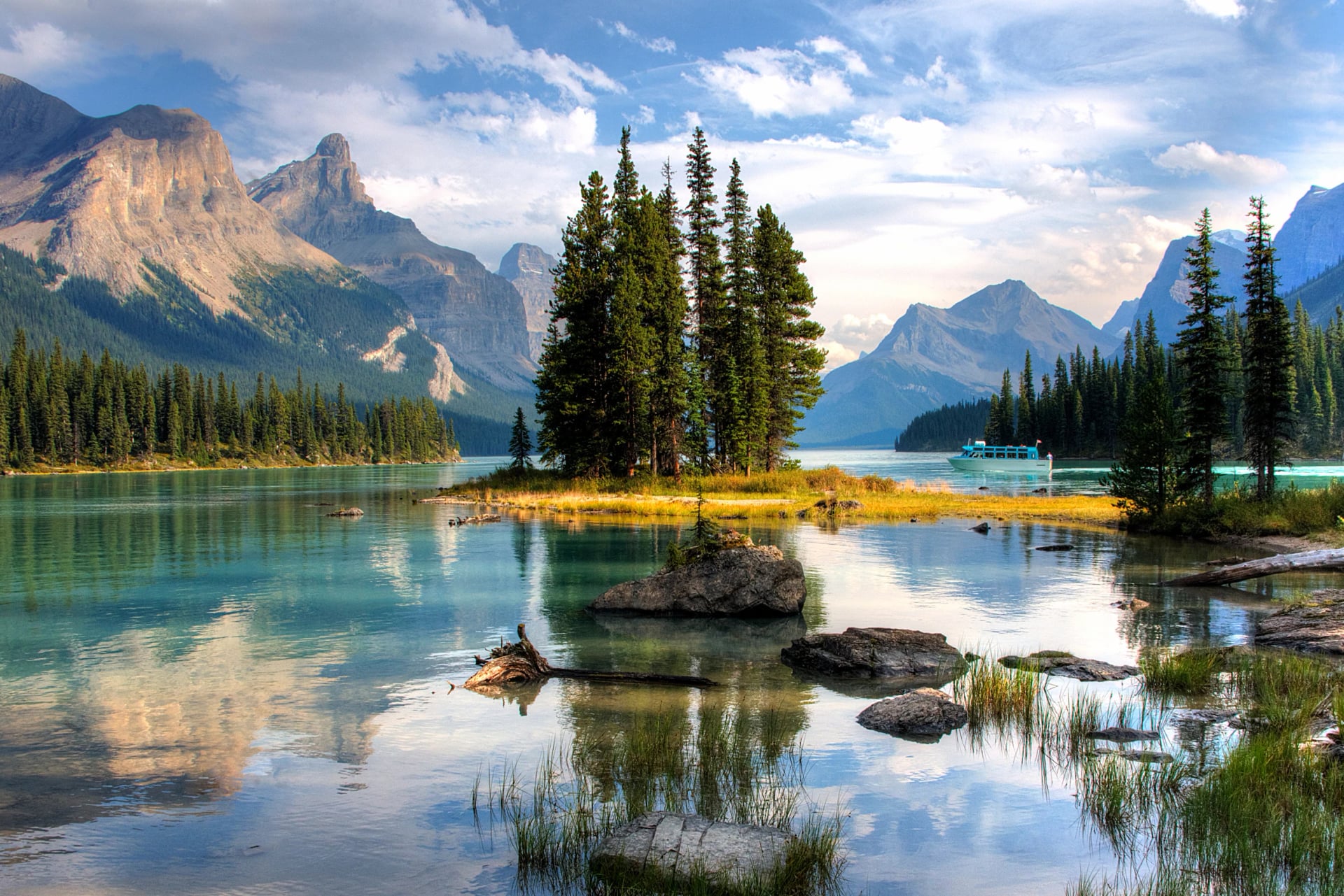 Spirit Island on Maligne Lake, a small tree-covered islet in turquoise water with snow-streaked peaks behind it.