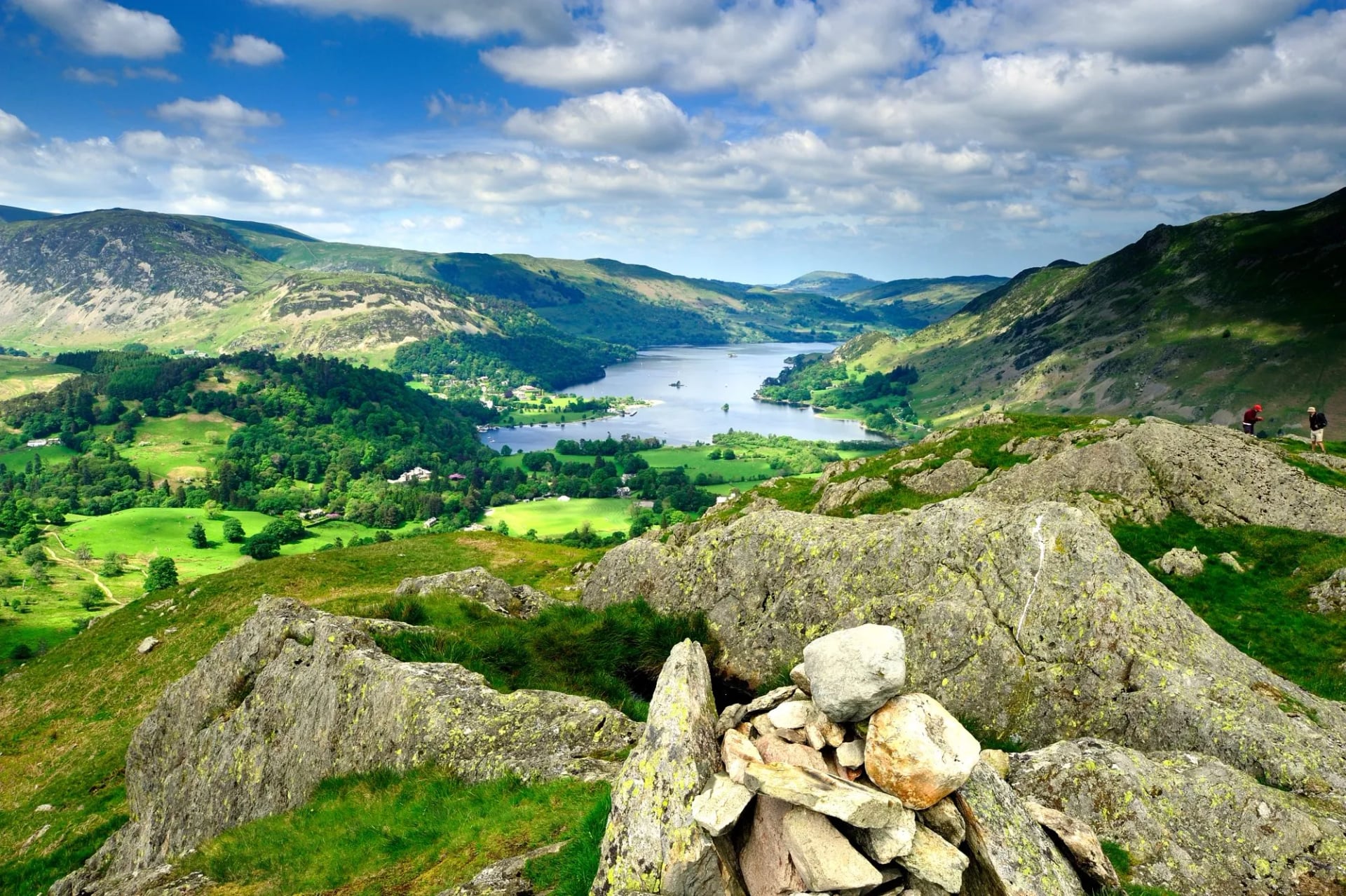 A slate cairn on a rocky top above a green valley and a lake