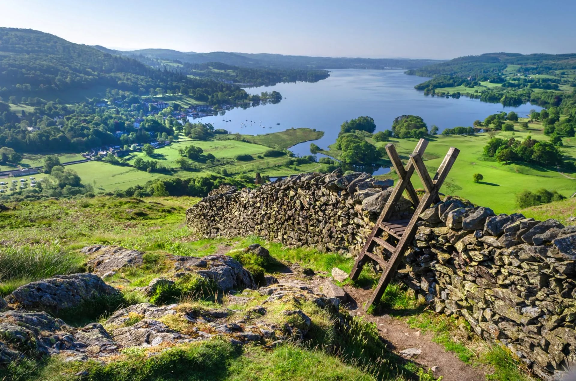 A wooden ladder stile over a drystone wall above a wooded lake
