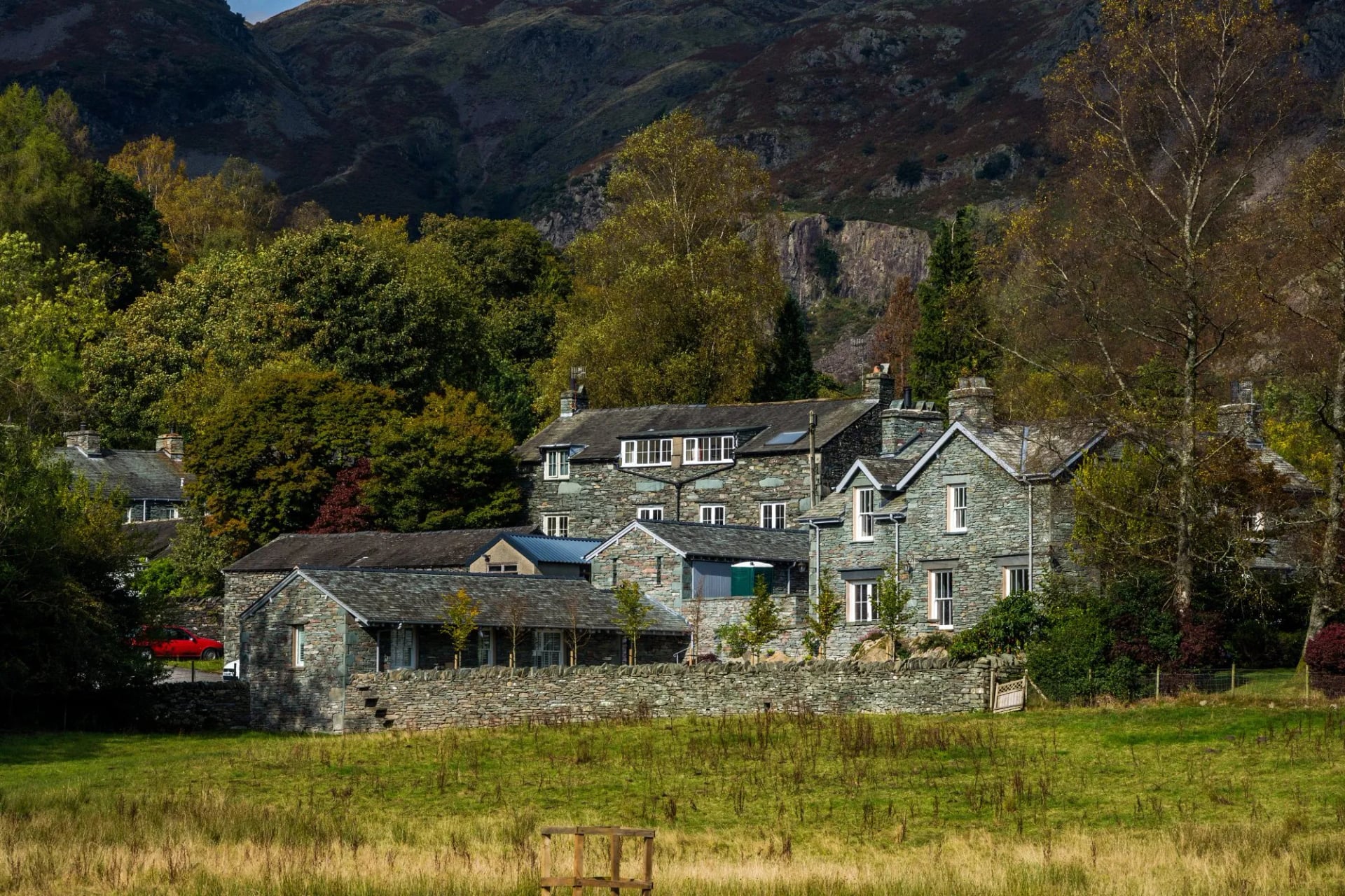 A large slate house among autumn trees below a crag at Elterwater