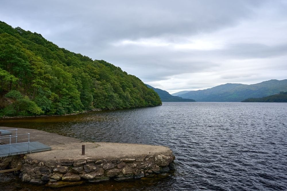 Loch Lomond fra en stenjetty med skovklædte bakker bagved
