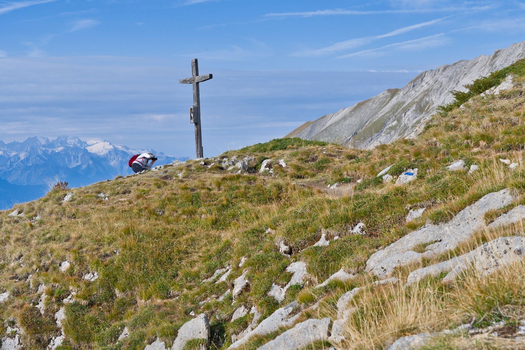 A walker resting beside a summit cross on an alpine ridge