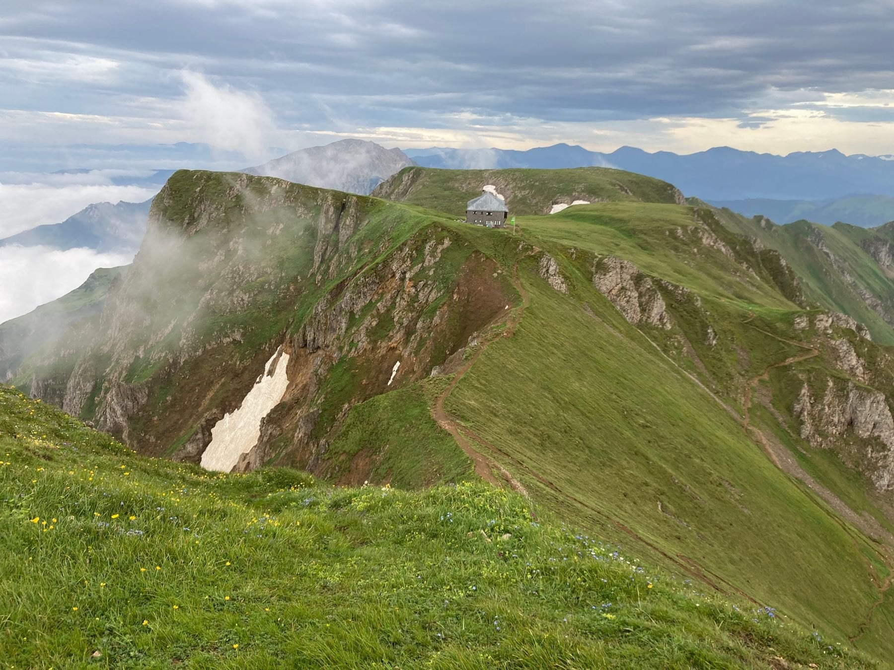A mountain hut on a green ridge with cloud below