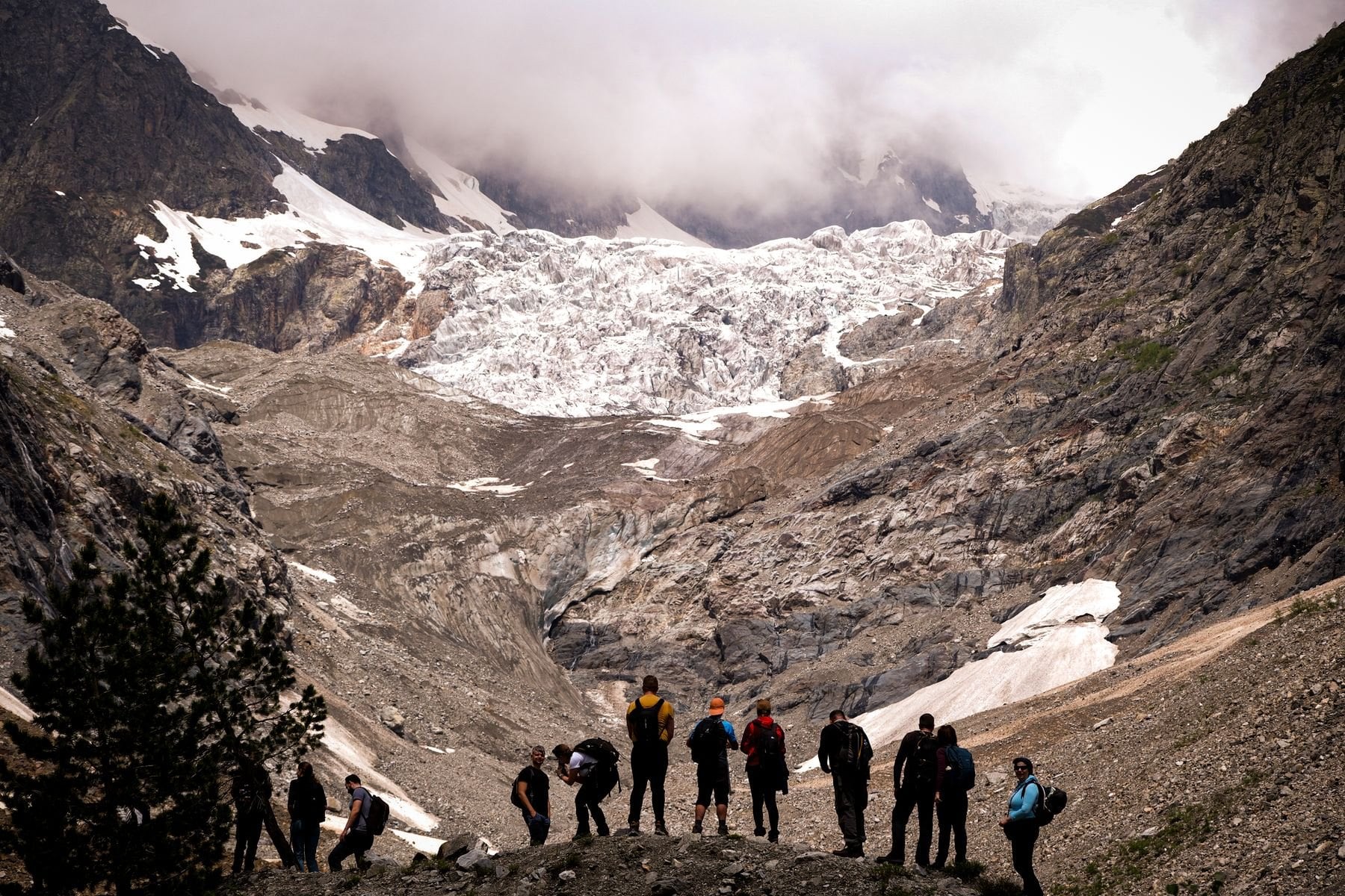 A group of walkers below a glacier in rugged mountains