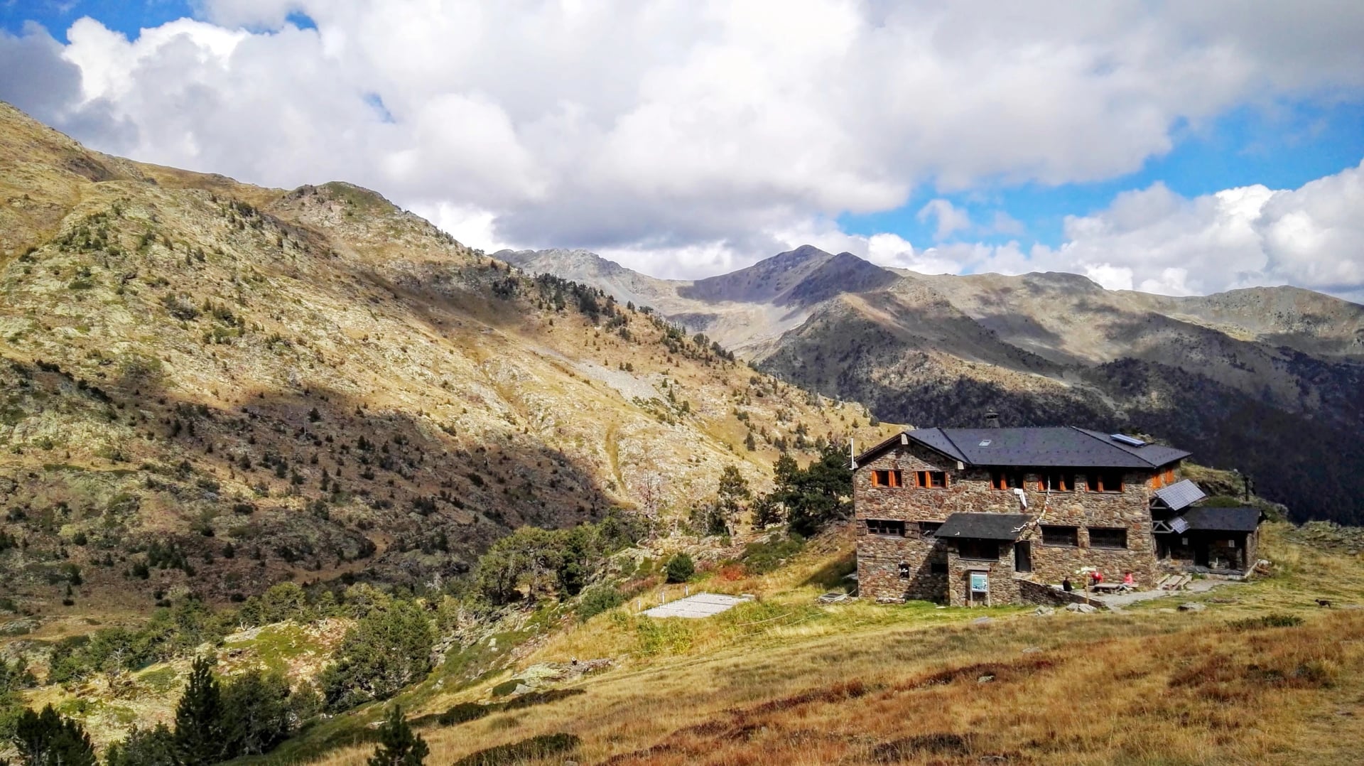 Stone mountain refuge on a green hillside below Andorran peaks