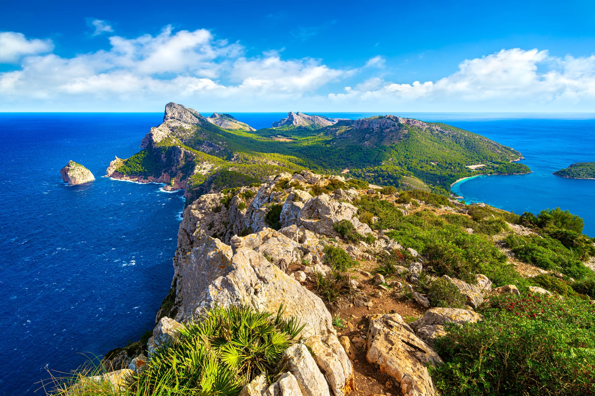 Rocky coastal peninsula with green hills extending into blue sea and sky with clouds