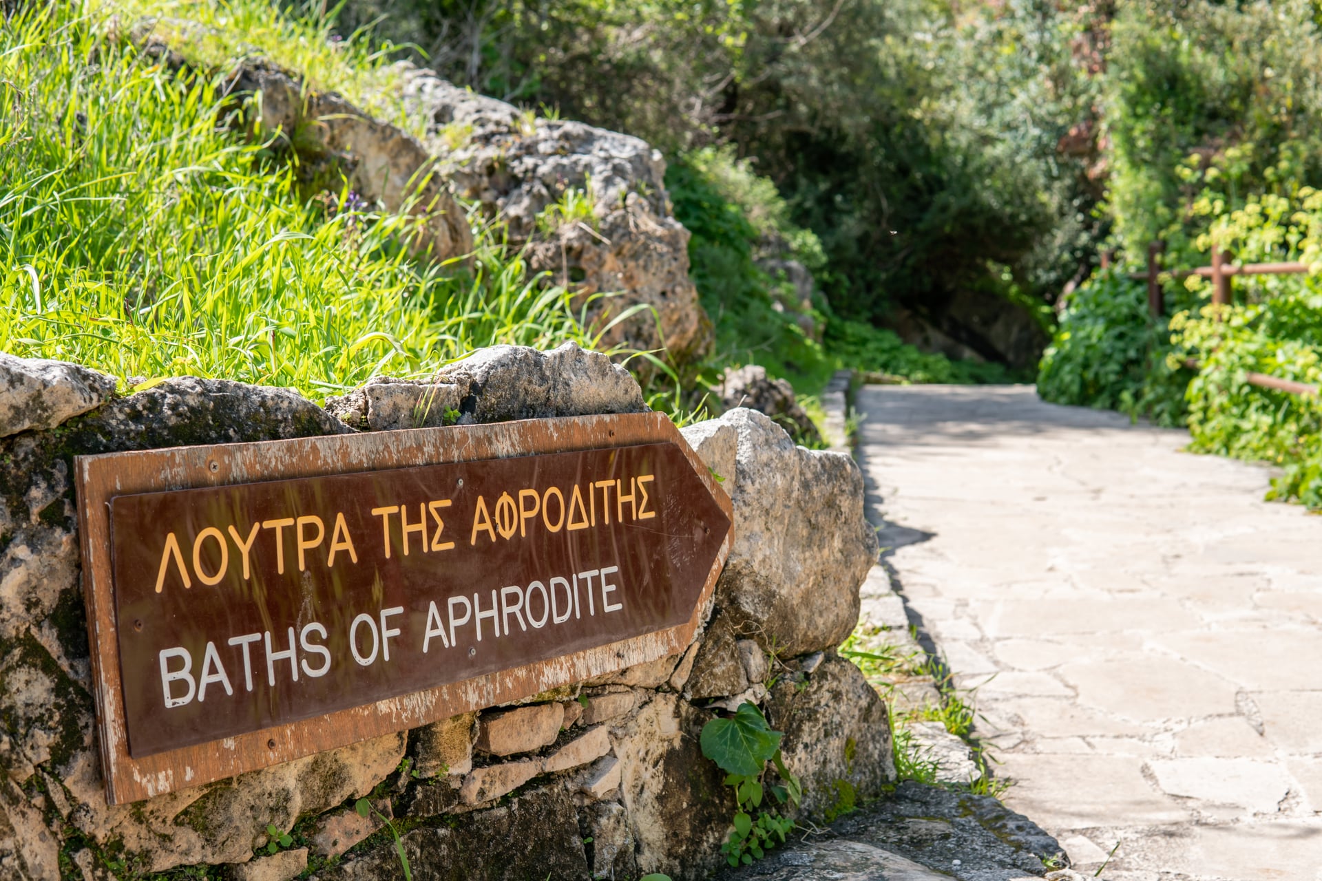 Baths of Aphrodite wooden directional sign on stone wall near walking path