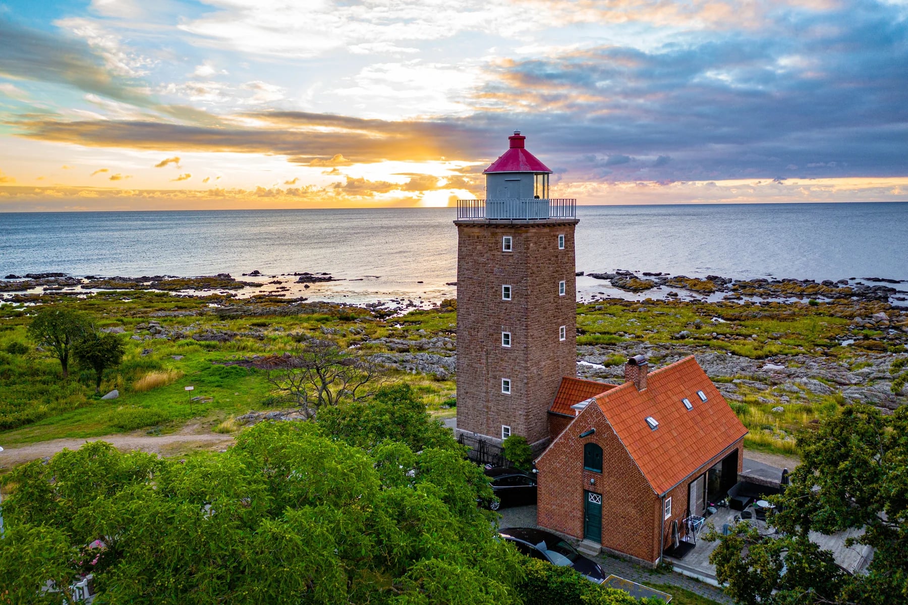 Un phare et des maisons à toit rouge sur une côte rocheuse dans la lumière douce du soir