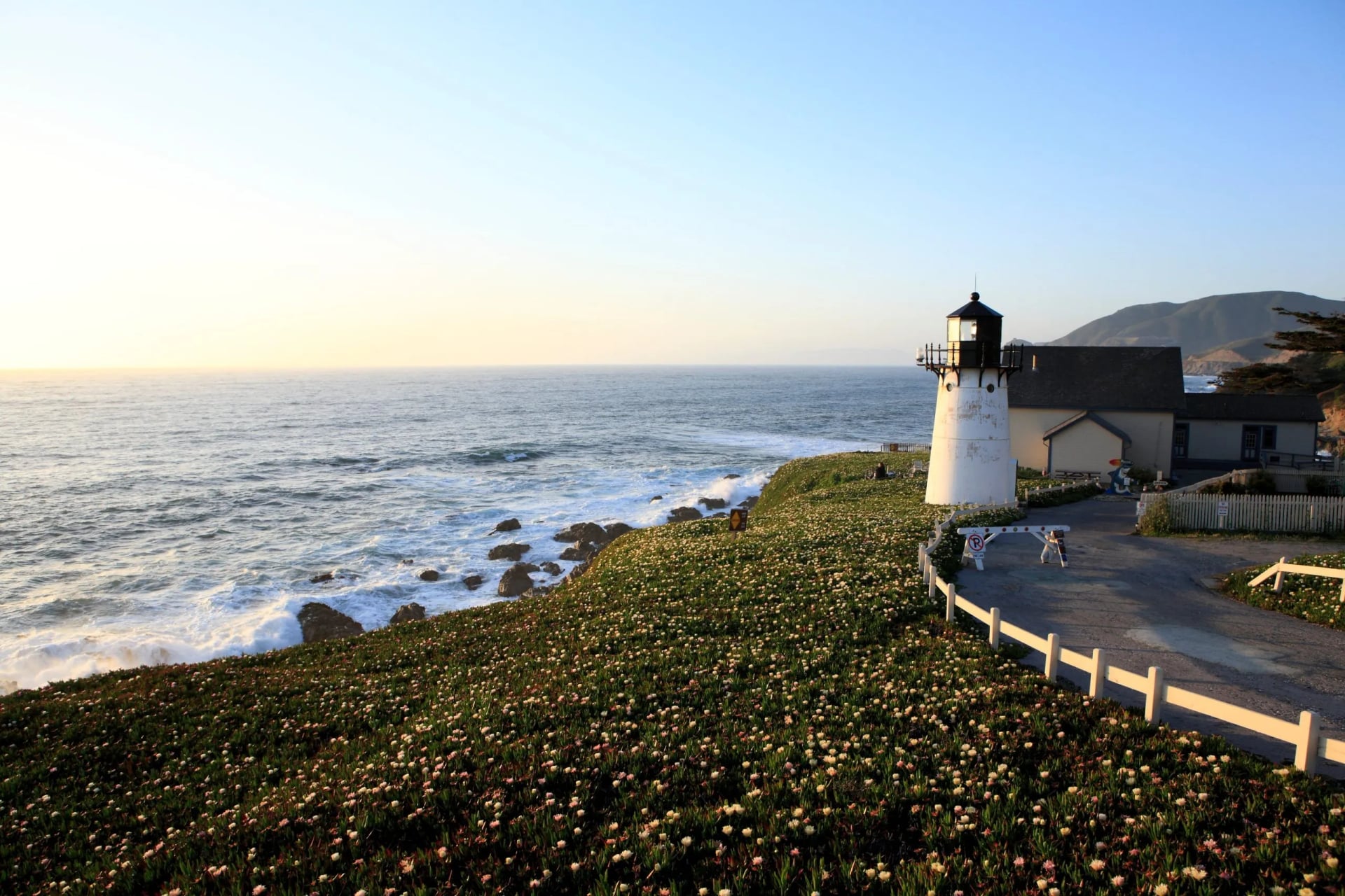 A white lighthouse on a low headland above a rocky shore at sunset