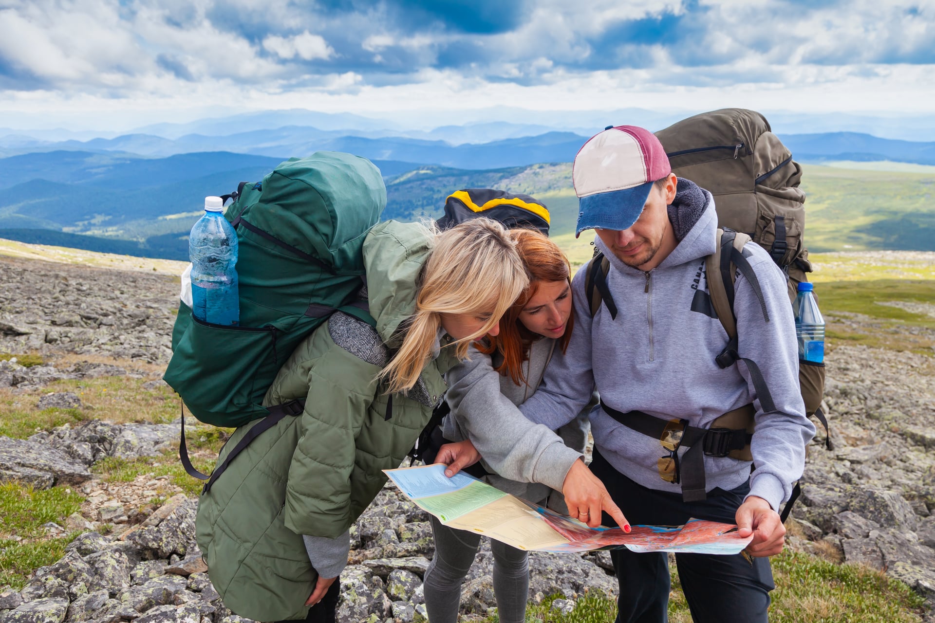 Tre vandrare med ryggsäckar som läser en karta på en bergstopp
