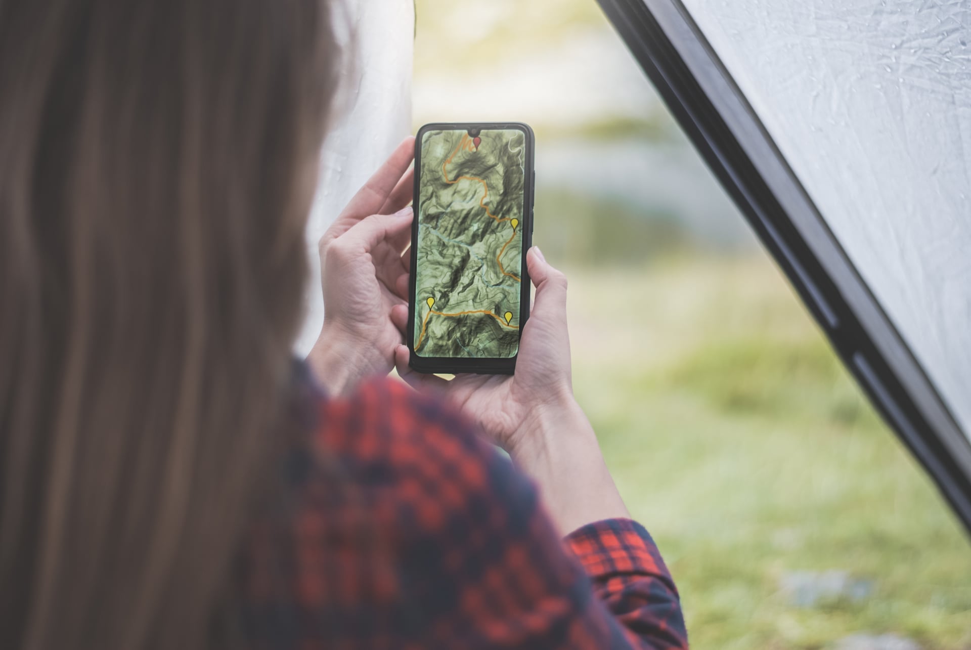 Person som håller smartphone med vandringskarta från insidan av ett tält