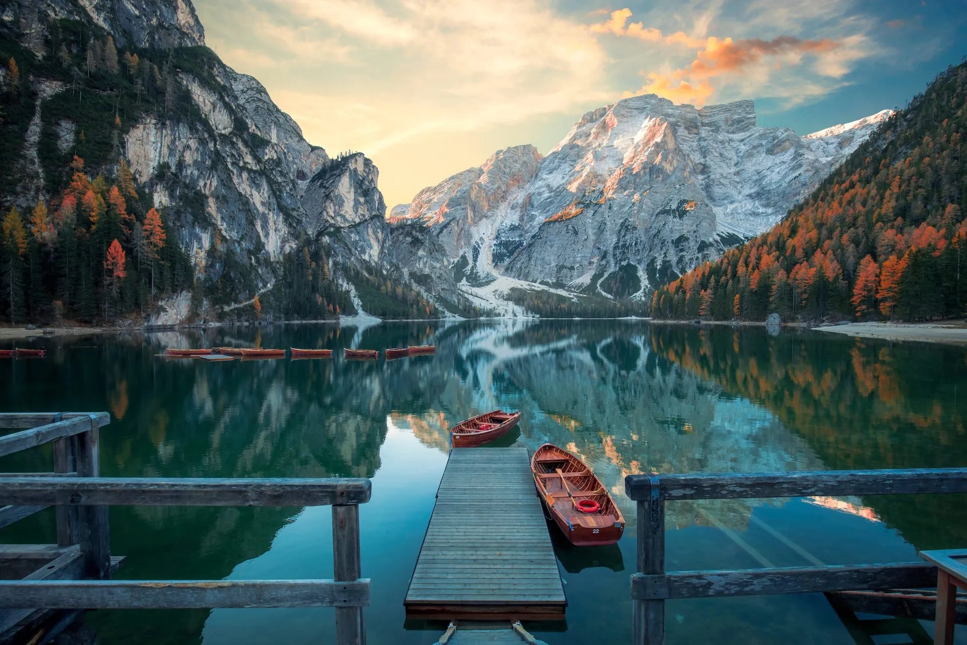 Wooden rowboats docked at a pier on Lago di Braies with reflections of autumn mountains.