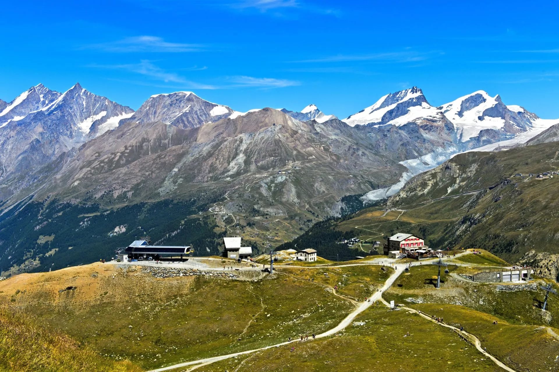Een berg hotel op een grasrijke richel met een brede sneeuwbedekte massa achter zich