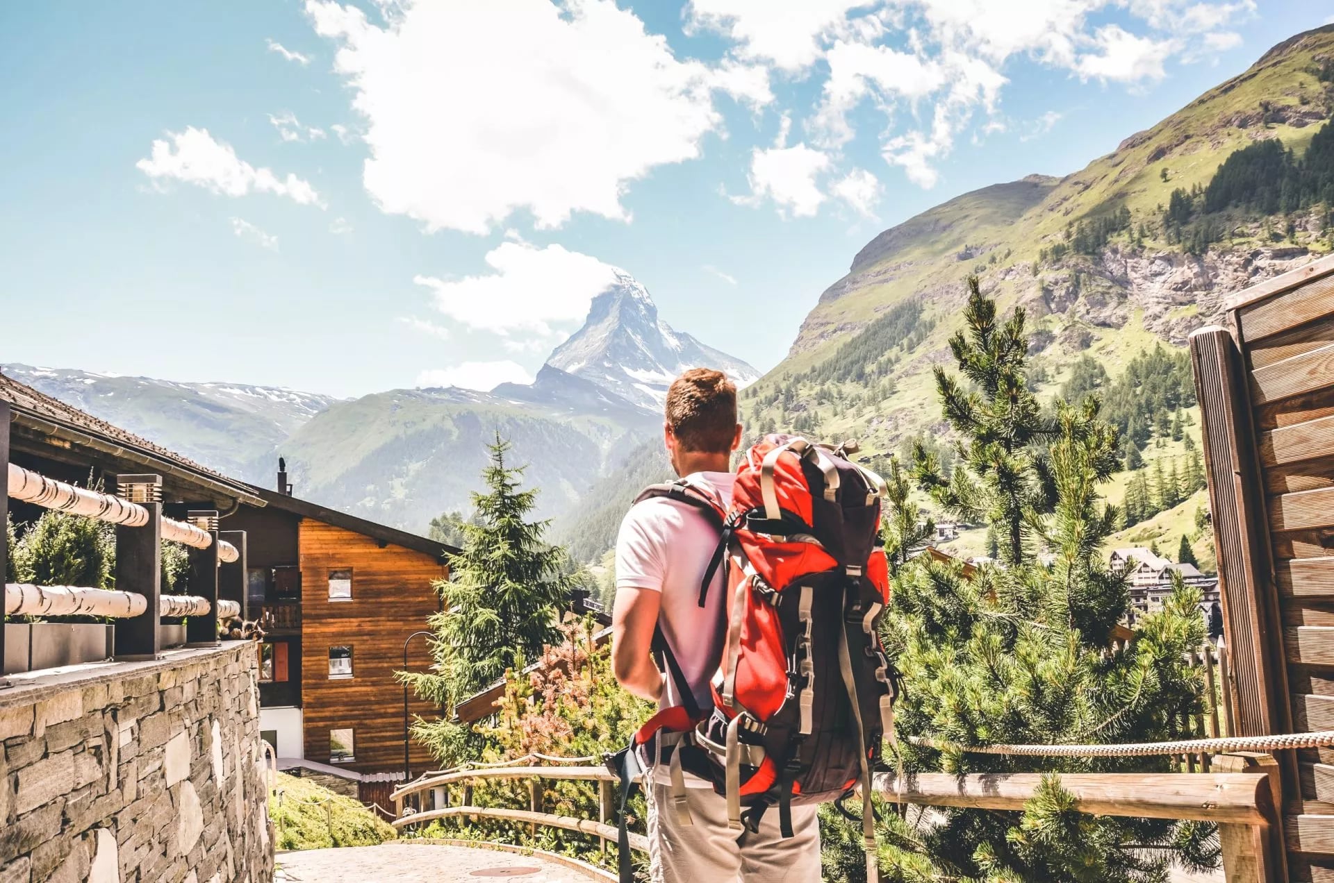 Een wandelaar met een grote rode rugzak die naar de Matterhorn kijkt vanaf een terras