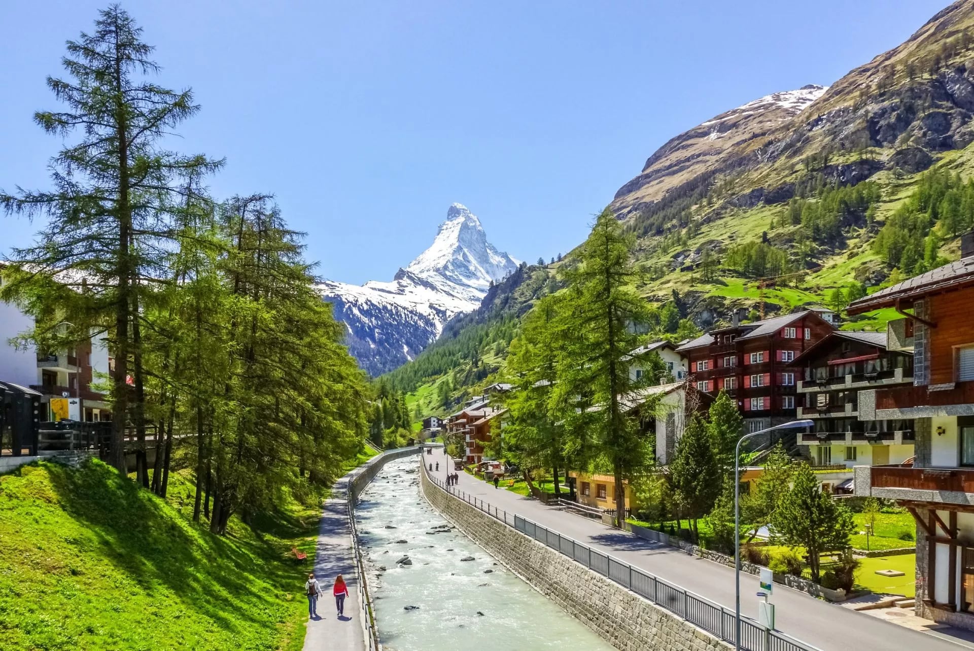 Een dorpsstraat naast een gekanaliseerde rivier met lorken en de Matterhorn op de achtergrond