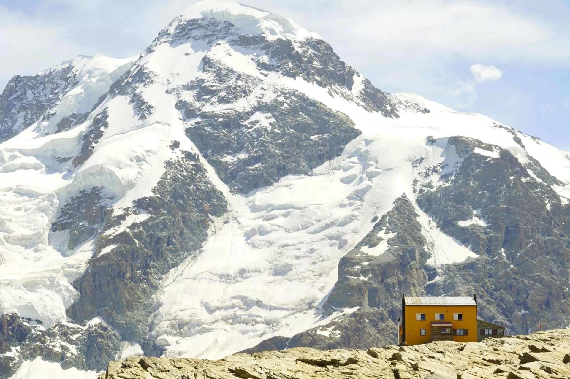 Een kleine gele hut op kale rots onder een brede met sneeuw bedekte wand