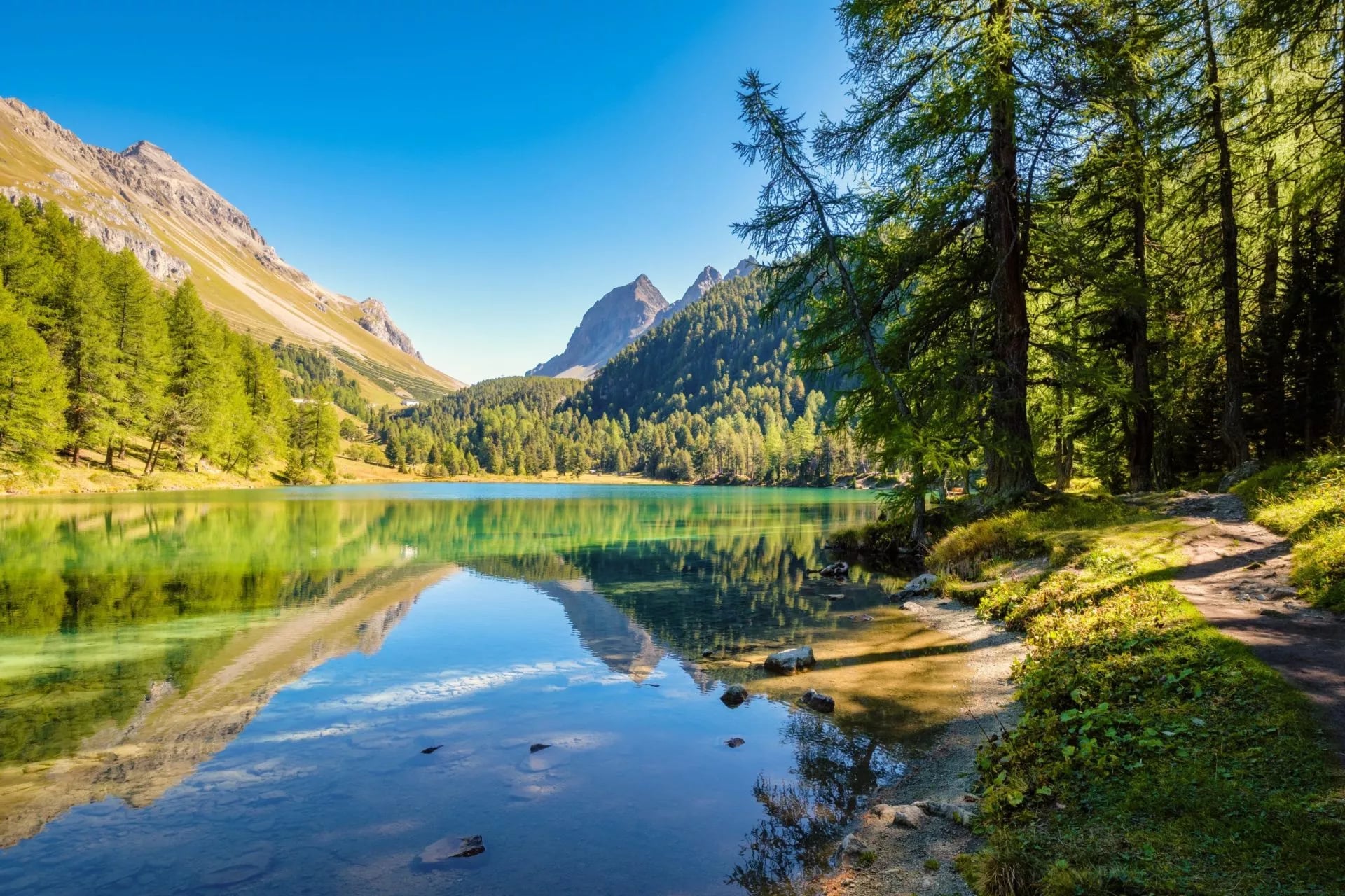 Klidné jezero odrážející modřínové stromy a hory v nízkém podzimním světle