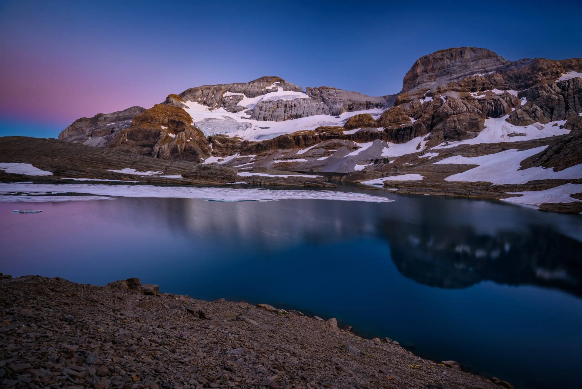 Still mountain lake holding the last of the snow under a pink dusk sky