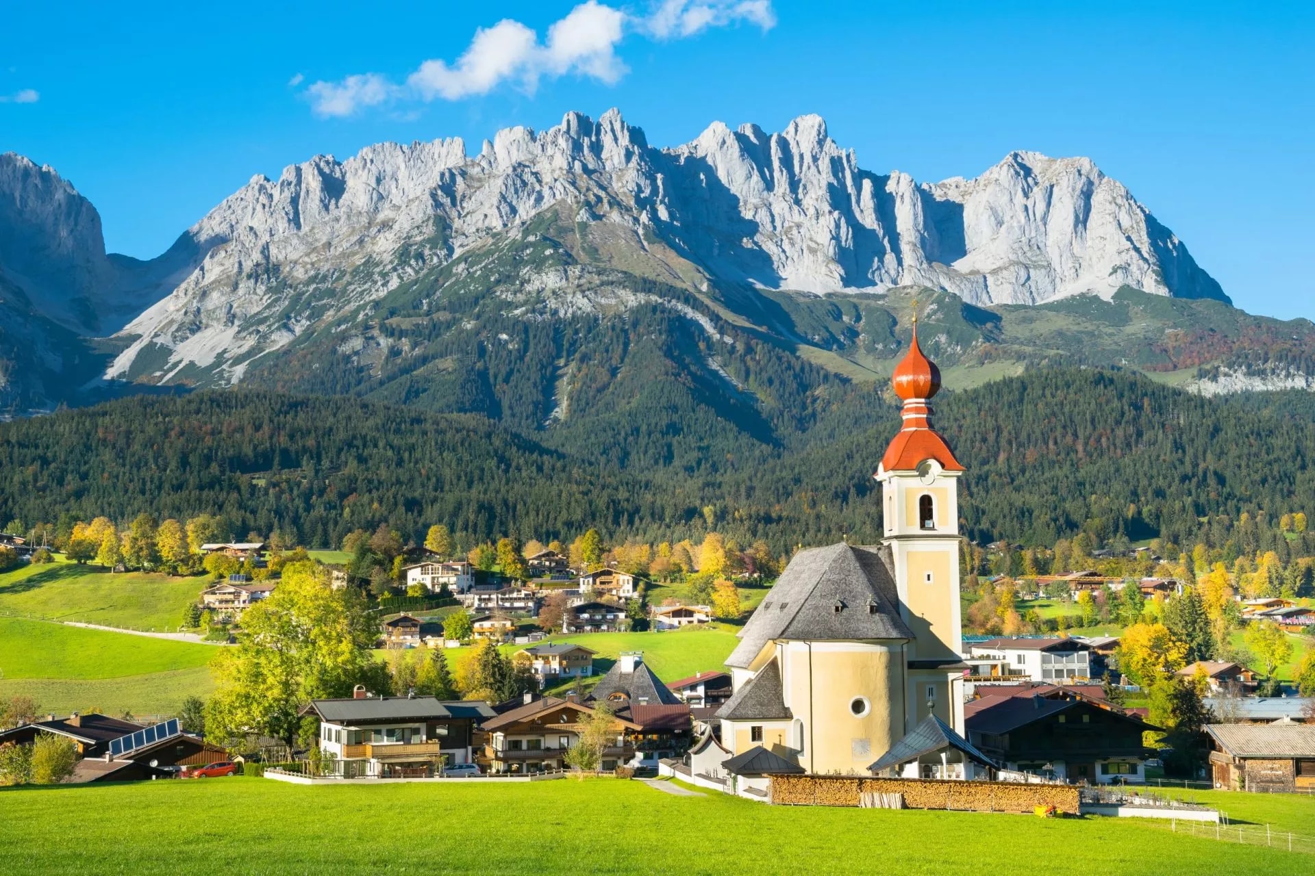 Alpine village with church, green meadows, and jagged mountains in Going am Wilden Kaiser.