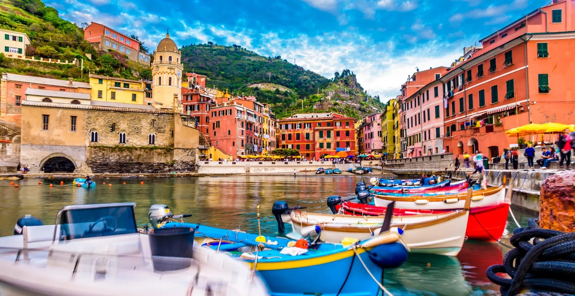 Colorful boats moored in harbor before hillside town with colorful buildings and church tower, Vernazza.