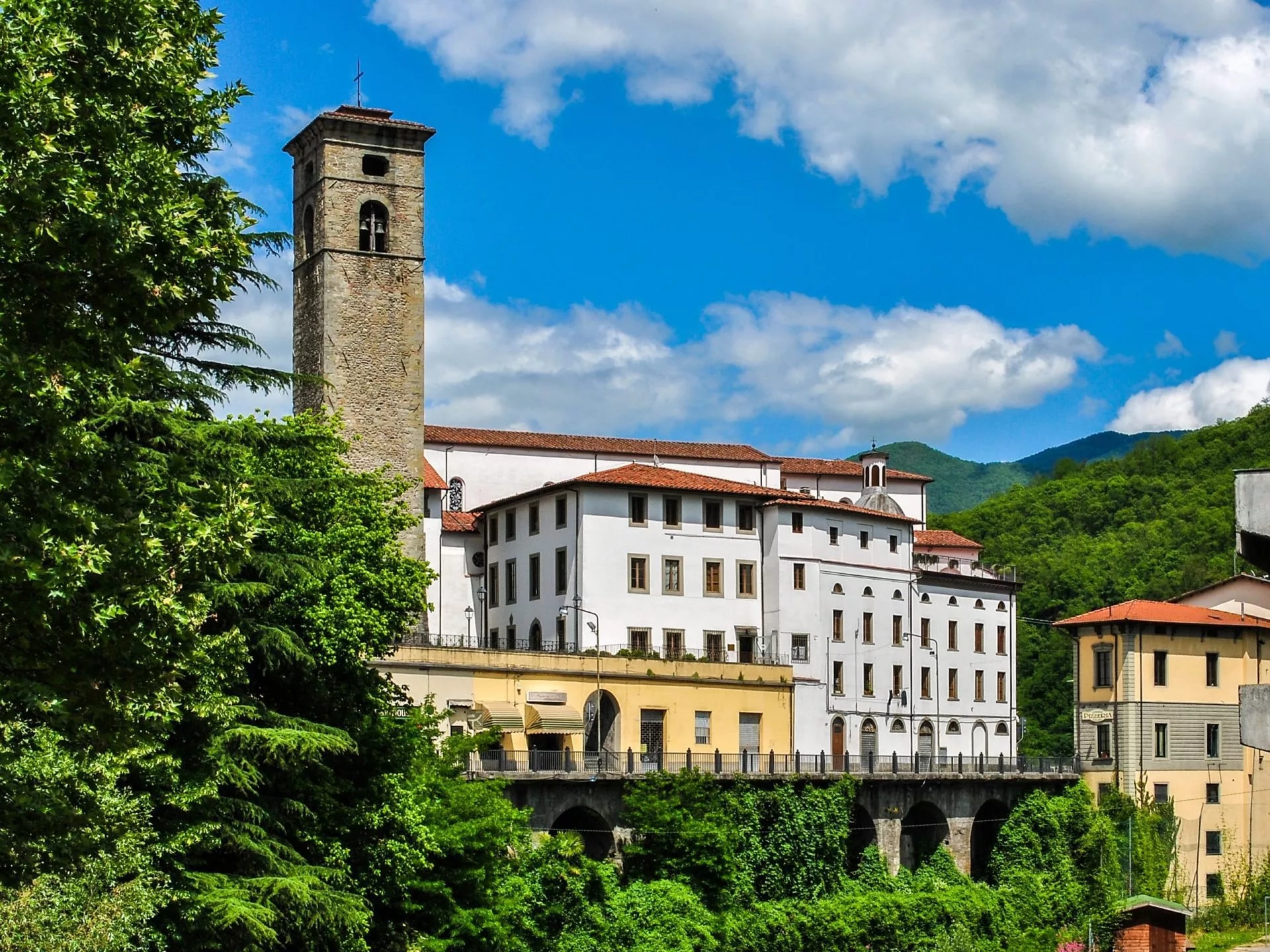 Stone medieval tower and white buildings above green foliage under a blue sky in Castelnuovo.
