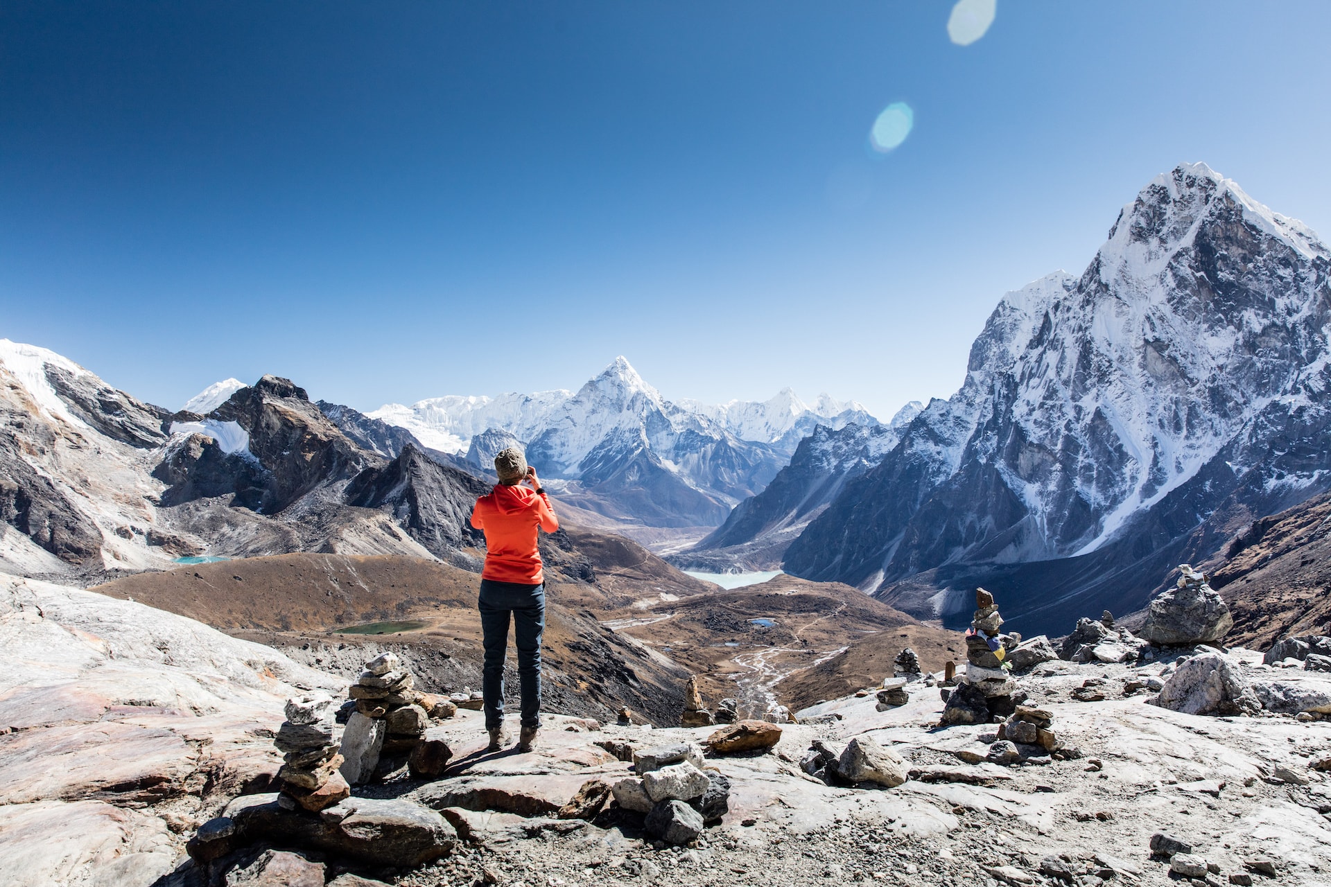 Hiker photographing snow-capped Himalayan mountains from Chola Pass viewpoint with cairns