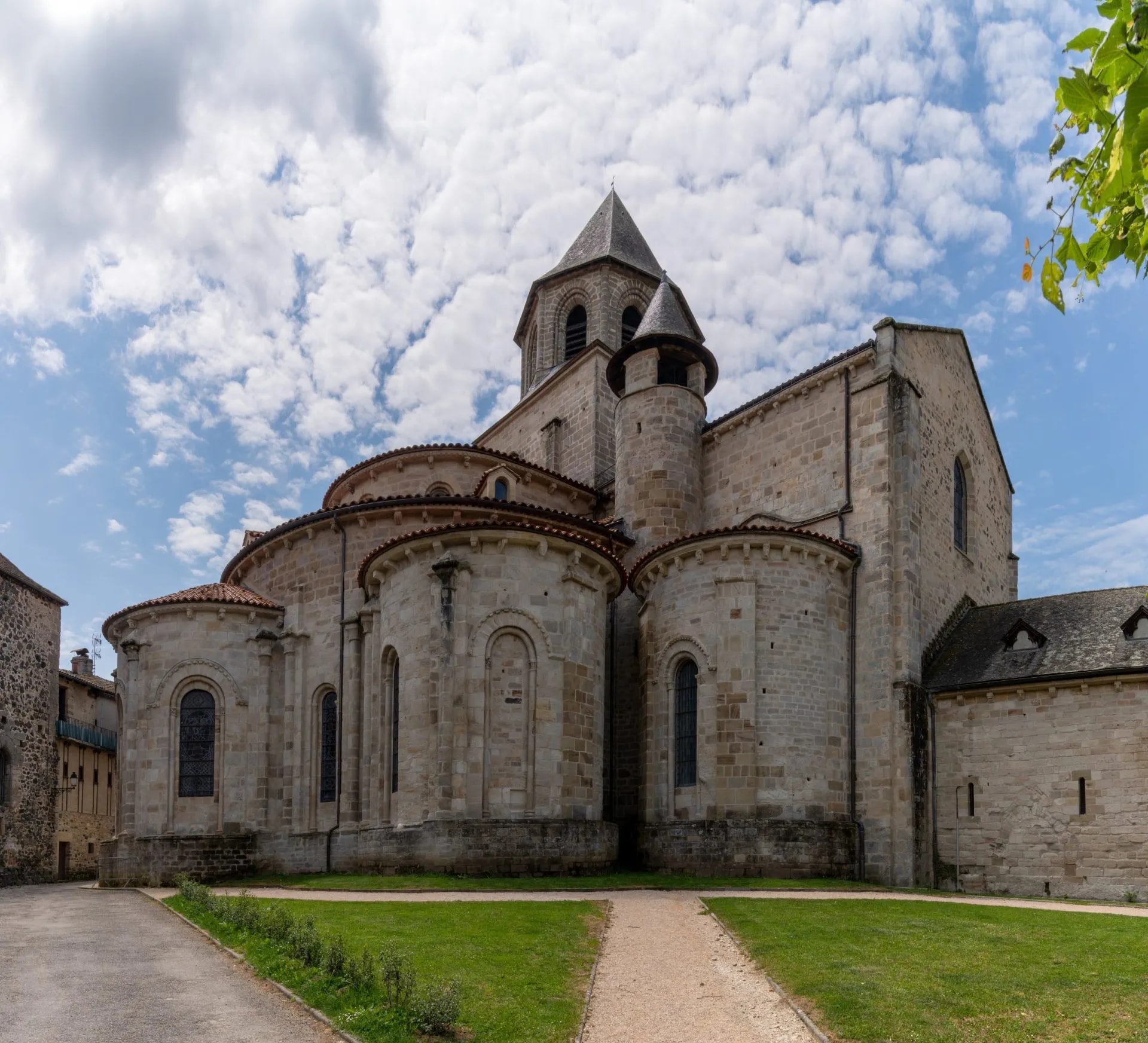 Romanesque stone abbey exterior with rounded apse and bell tower under a cloudy blue sky.