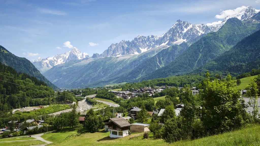Alpine village nestled in a valley with snow-capped mountains under a blue sky, Les Houches.