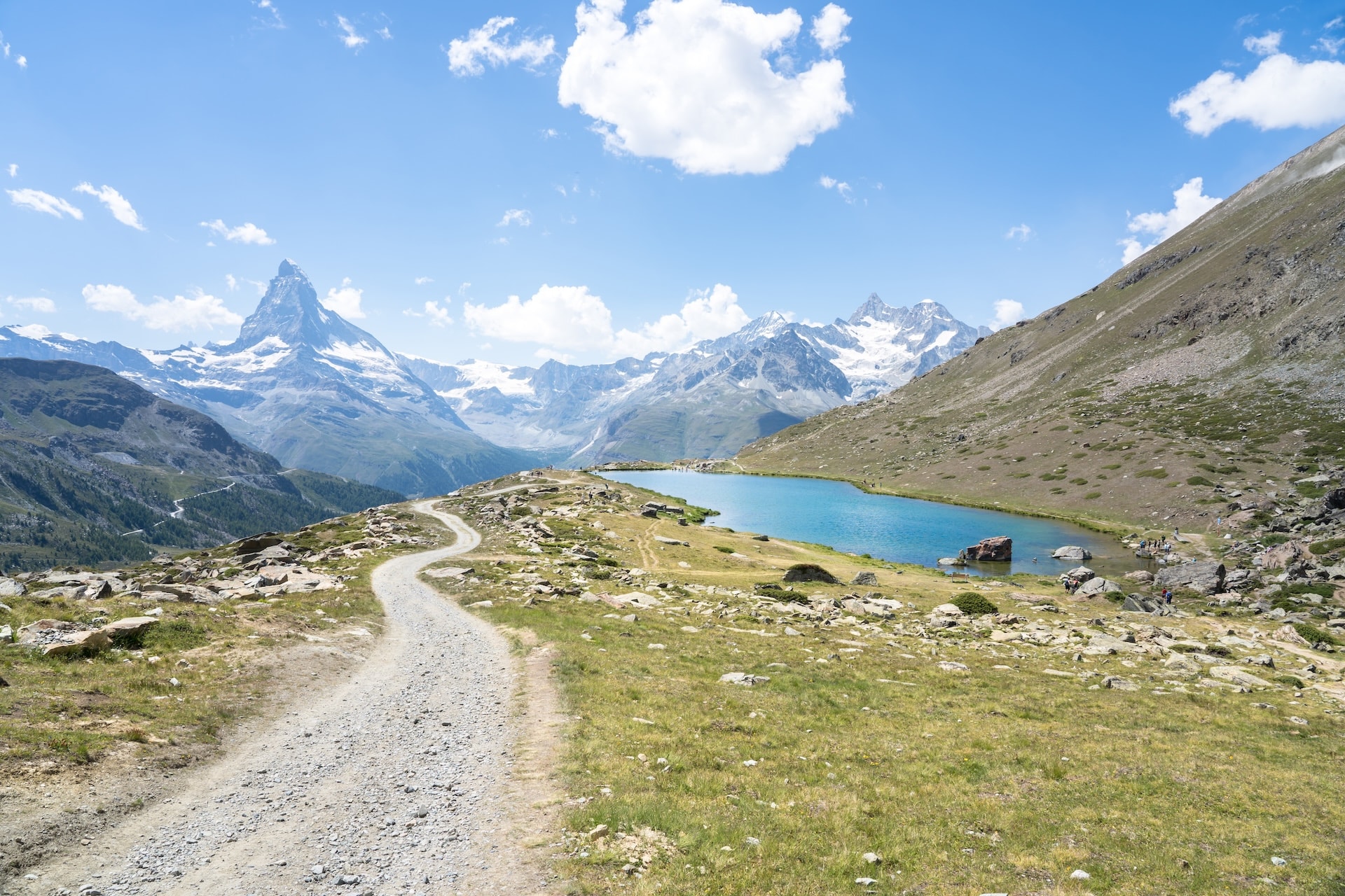 Hiking trail winding past Stellisee lake with Matterhorn peak and snowy Alps in background
