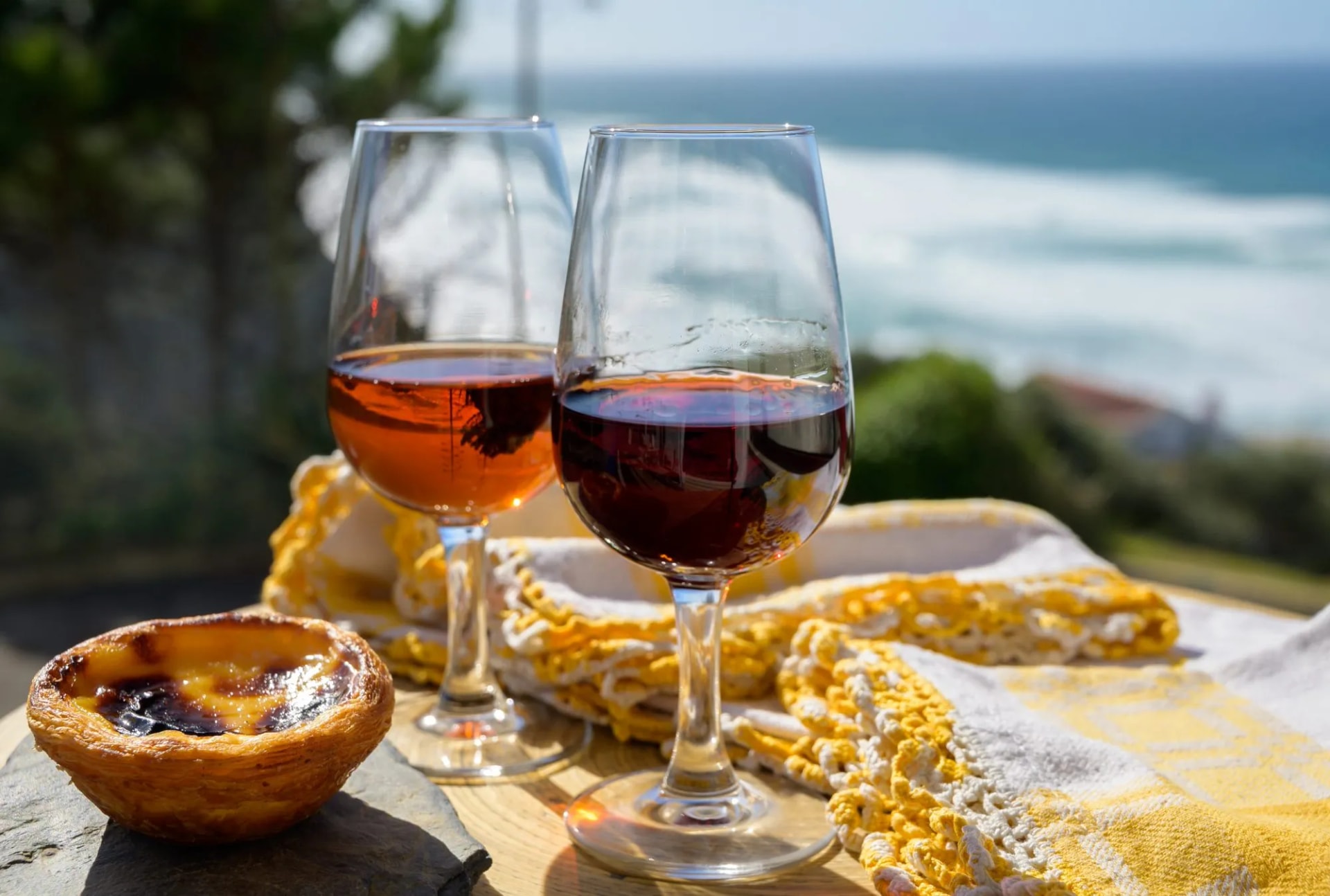 Portugal's traditional food and drink, glass of porto wine, muscatel and sweet dessert Pastel de nata egg custard tart pastry served with view on blue