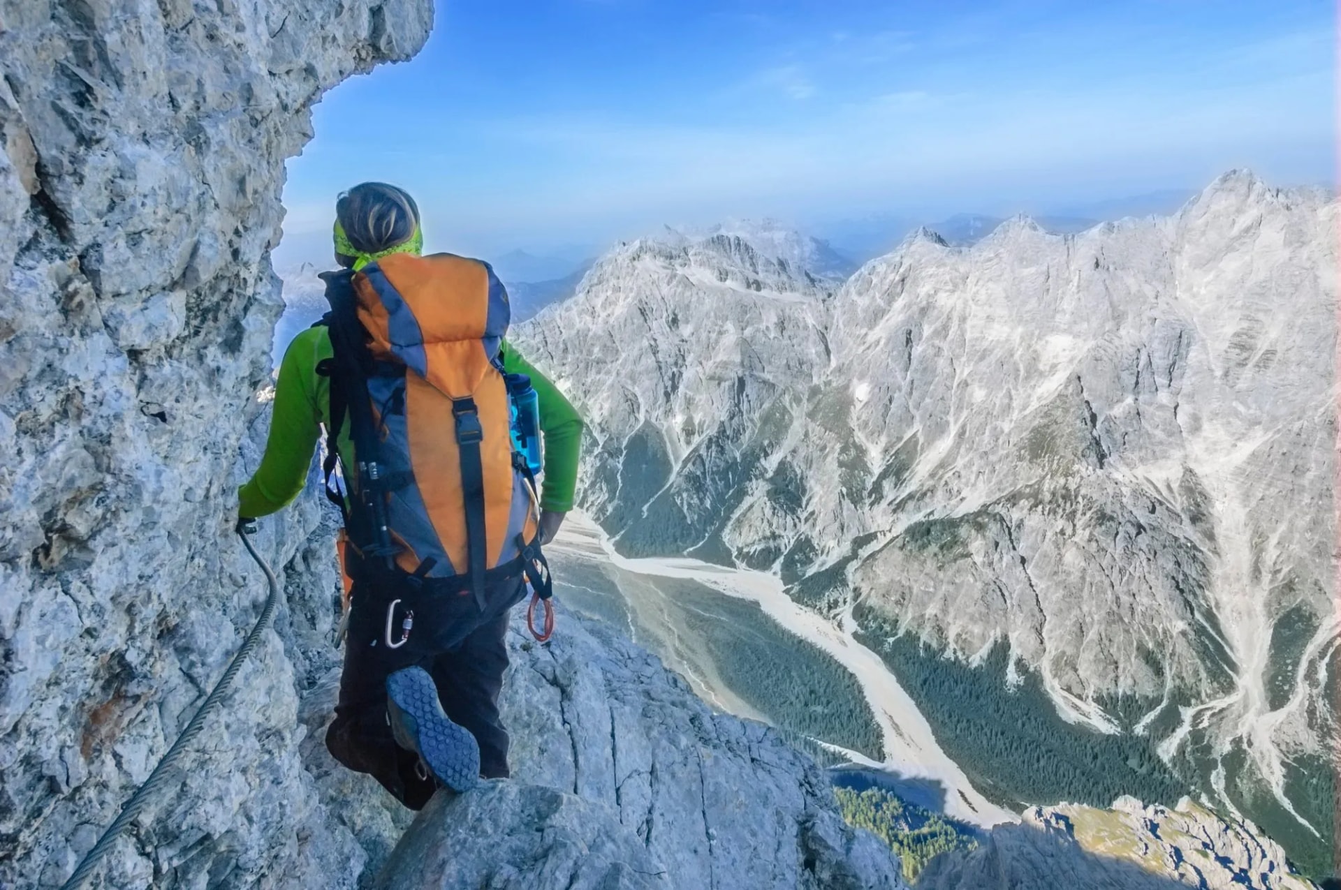 Via Ferrata climber ascending steep rock face with view of rugged Watzmann mountains.