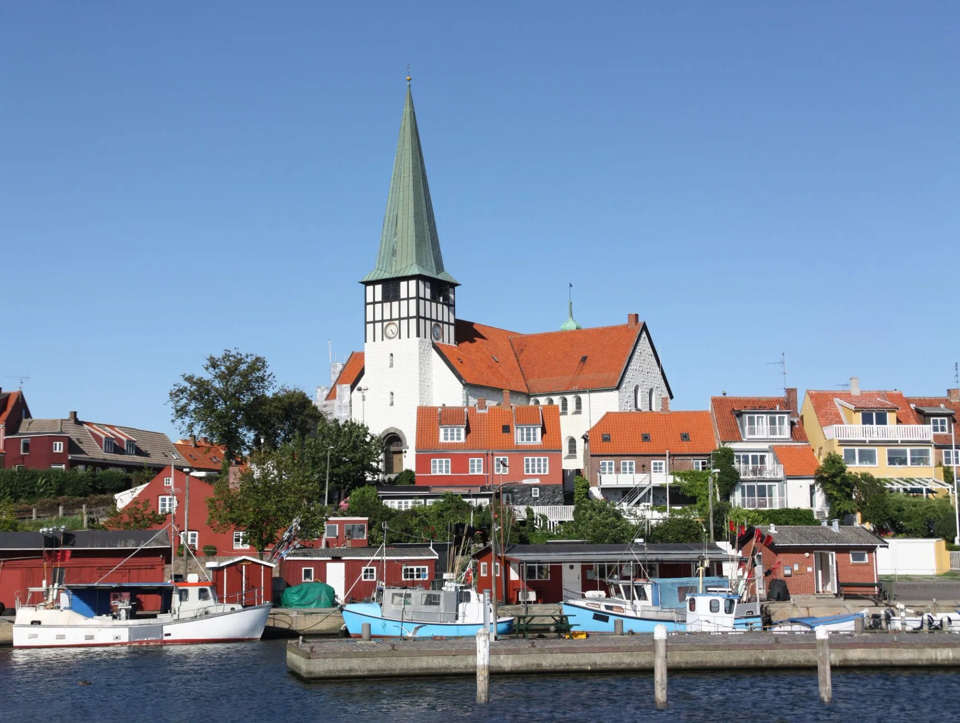 Fishing boats are in the harbor in the small town of Rønne on the Danish island of Bornholm in the Baltic Sea. In the background the historic white church of the city and several colorful houses.
