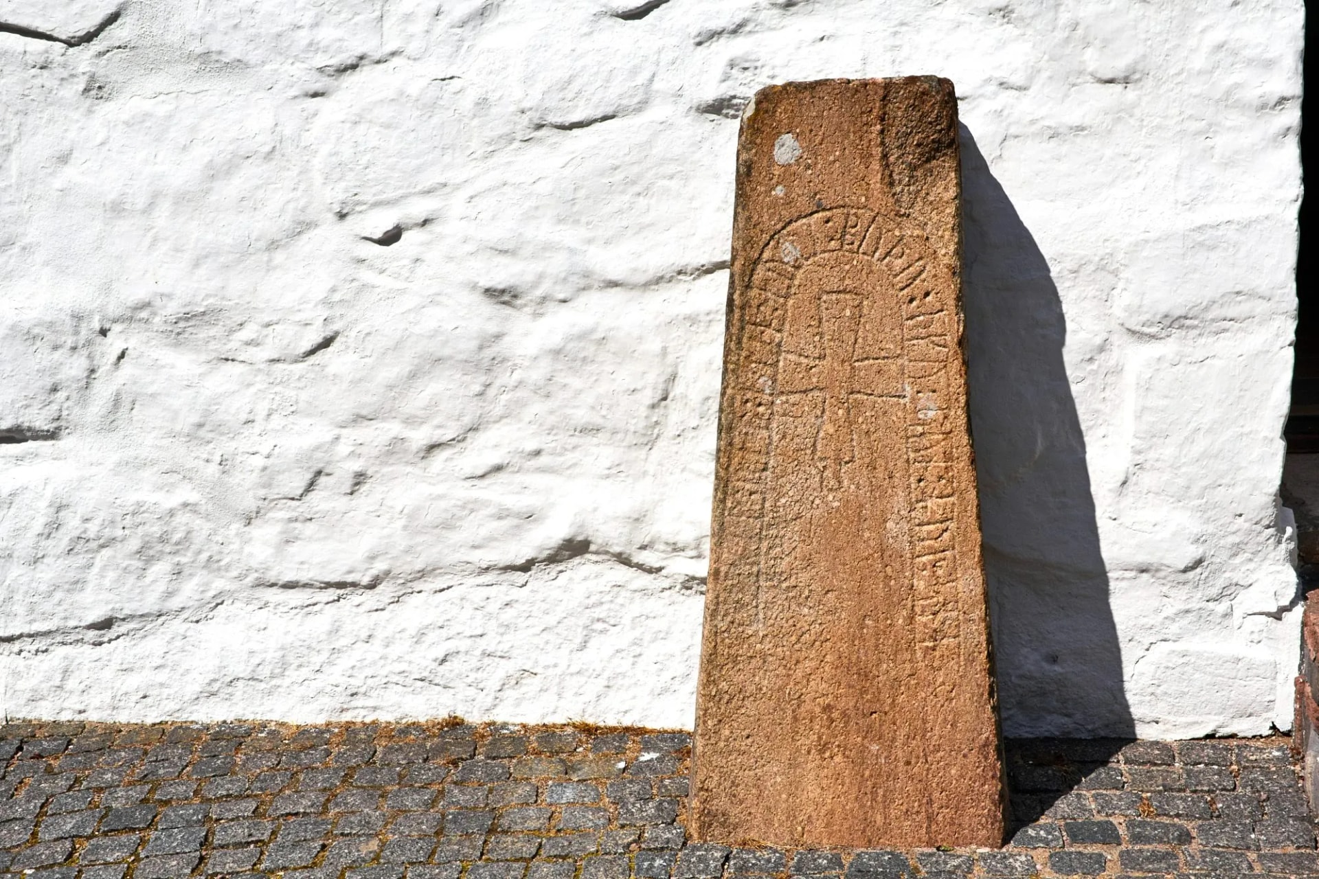 Rune stone with carvings standing against a white textured wall on cobblestones, Osterlars.