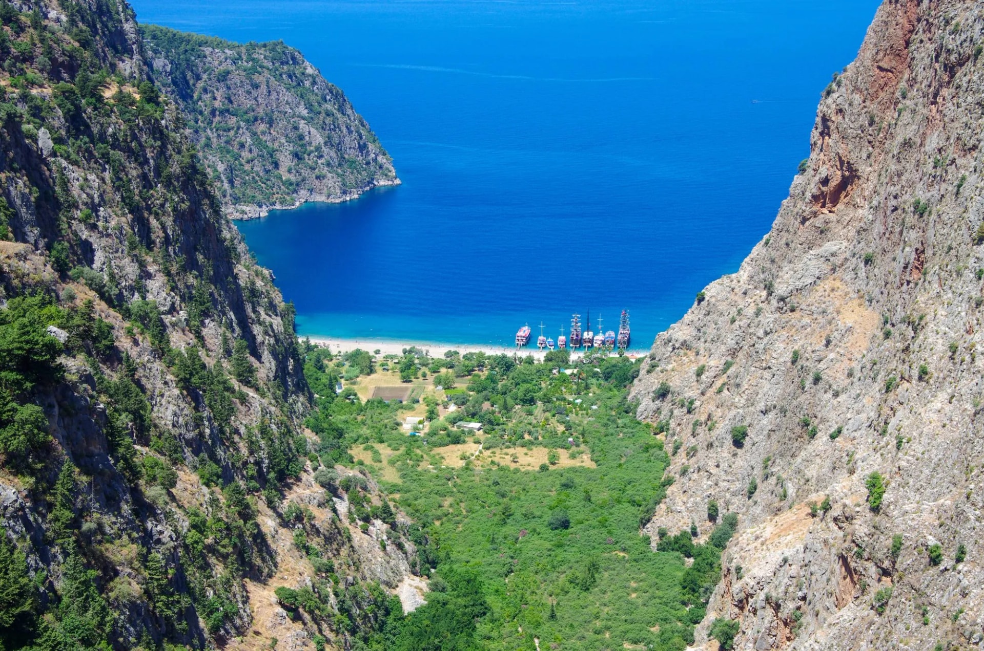 Valley opening to beach with boats anchored in bright blue sea between steep cliffs