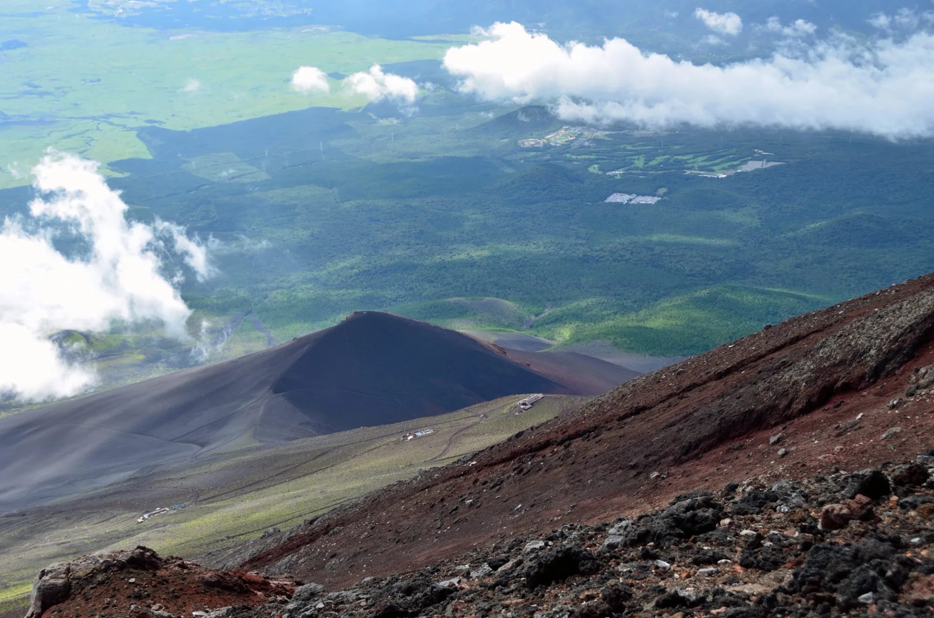 View from the top of Mt. Fuji showing volcanic slopes, green valleys, and clouds below