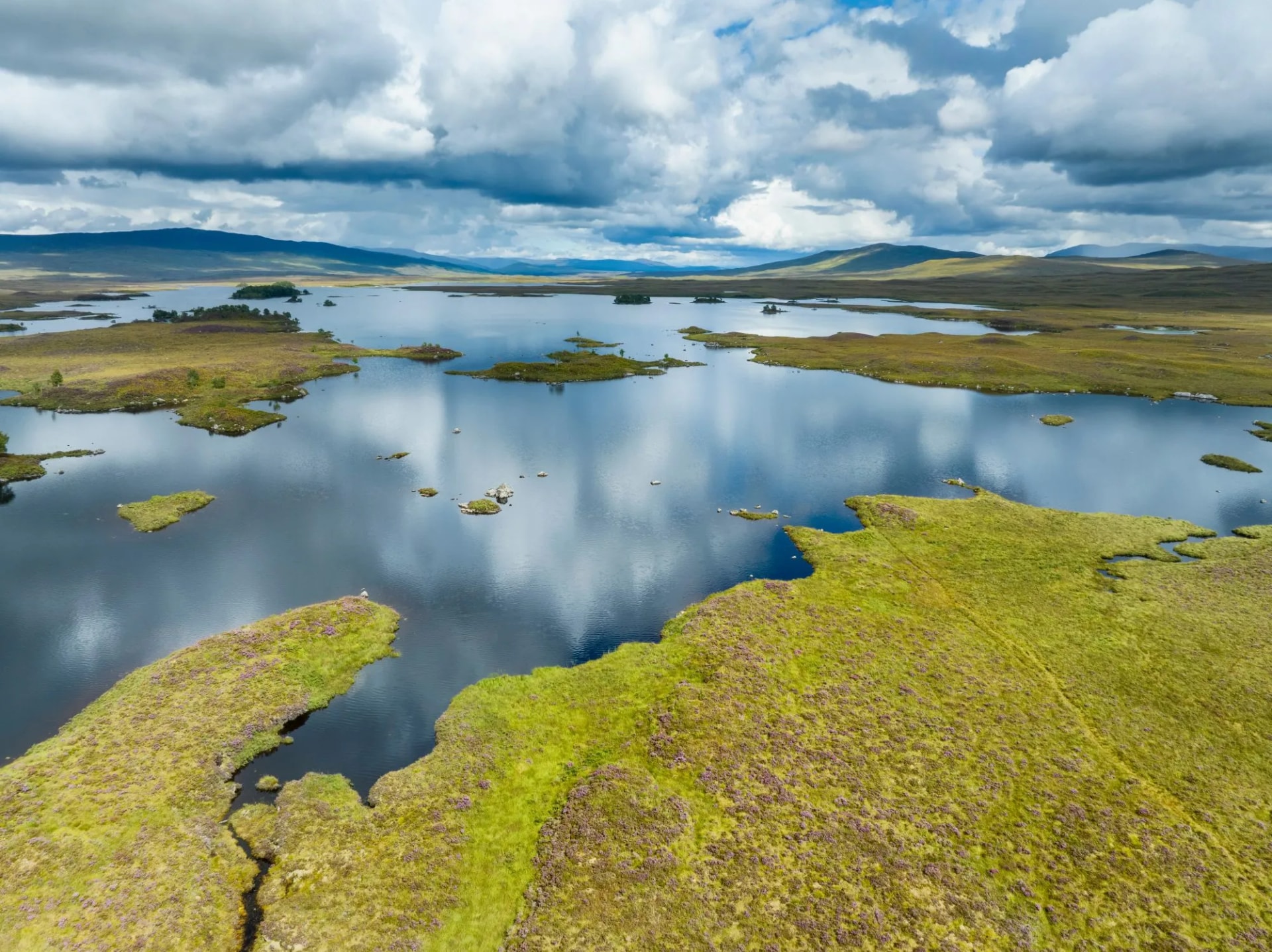 Vast moorland lake with small islands reflecting dramatic cloudy sky and distant hills