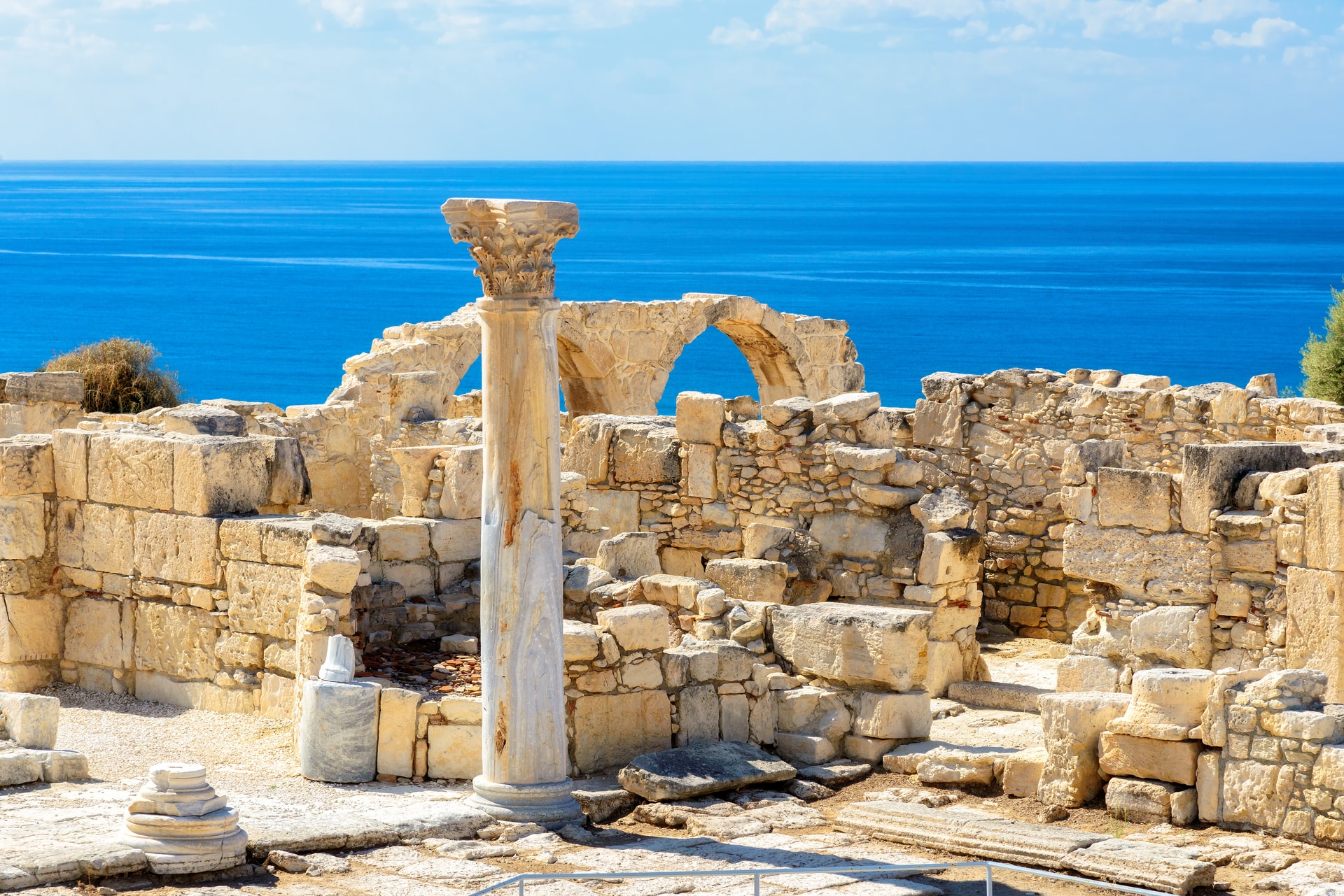 Ancient stone ruins with a column fragment overlooking the bright blue Mediterranean Sea in Paphos.