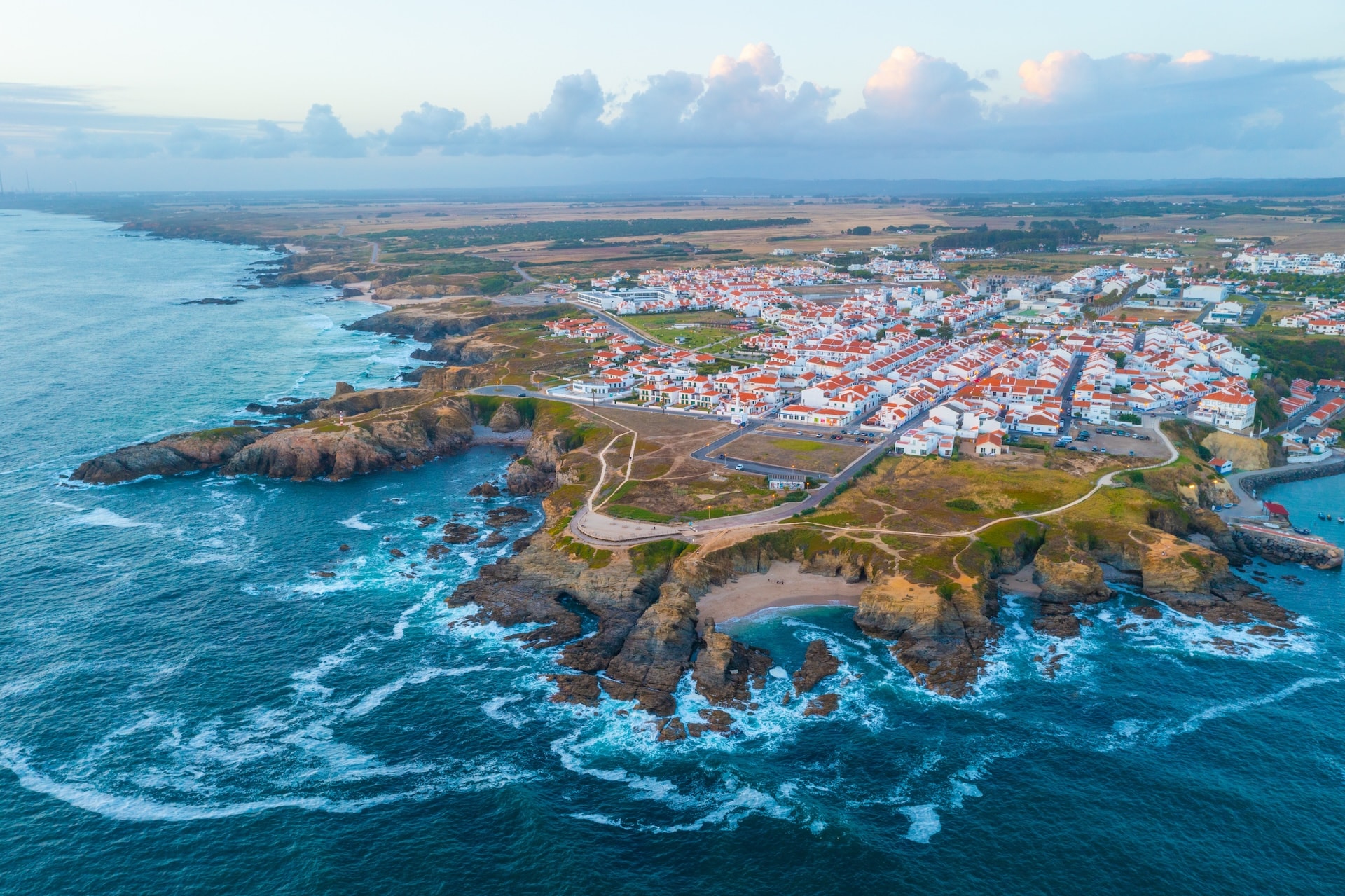 Aerial view of Porto Covo town with white buildings and orange roofs on rocky coastline in Portugal.