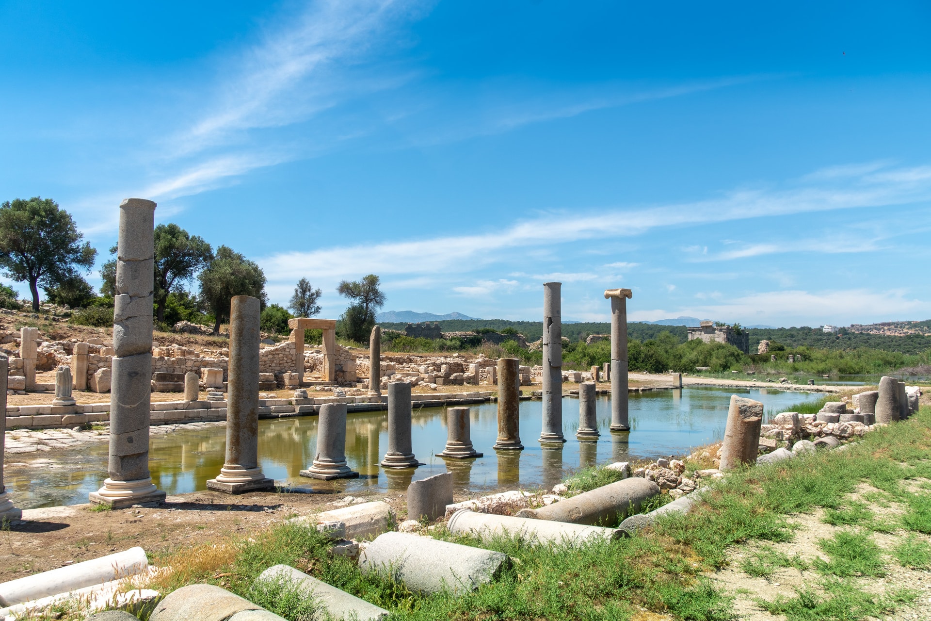 Ancient stone columns standing in water at the Patara ruins under a bright blue sky.
