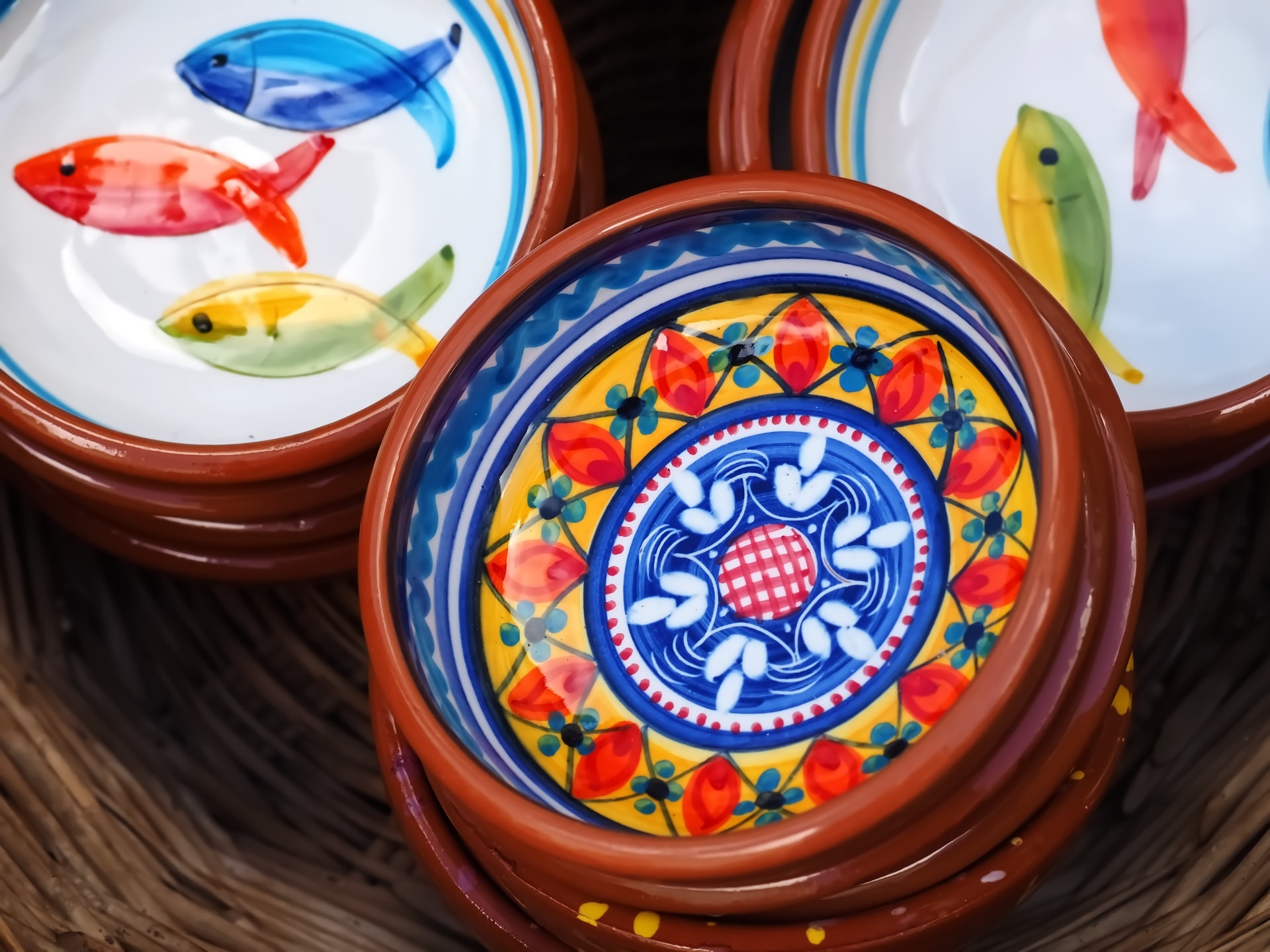 Colorful Portuguese ceramic bowls with fish and floral designs stacked in a woven basket.